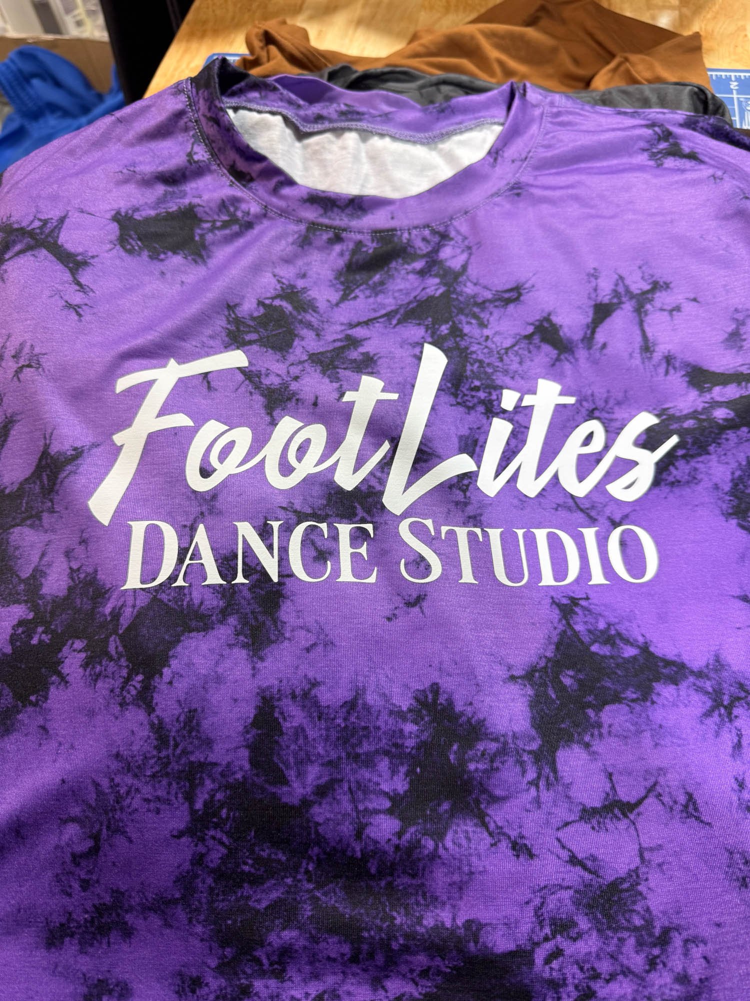 Purple tie-dye T-shirt with white text that reads 'FootLites DANCE STUDIO'.