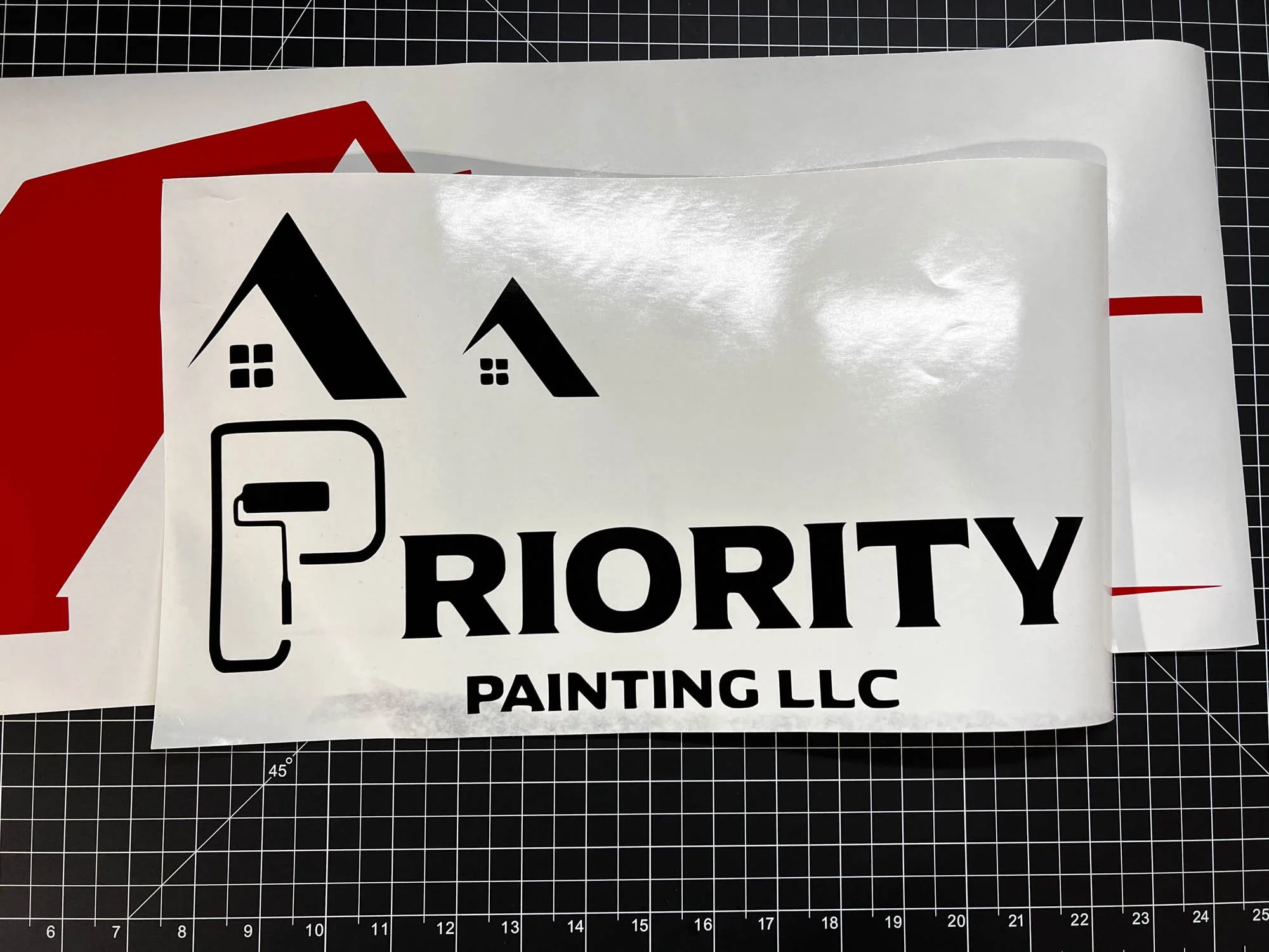 A sticker with a house icon, a paint roller icon, and the text 'PRIORITY PAINTING LLC' on a black cutting mat.