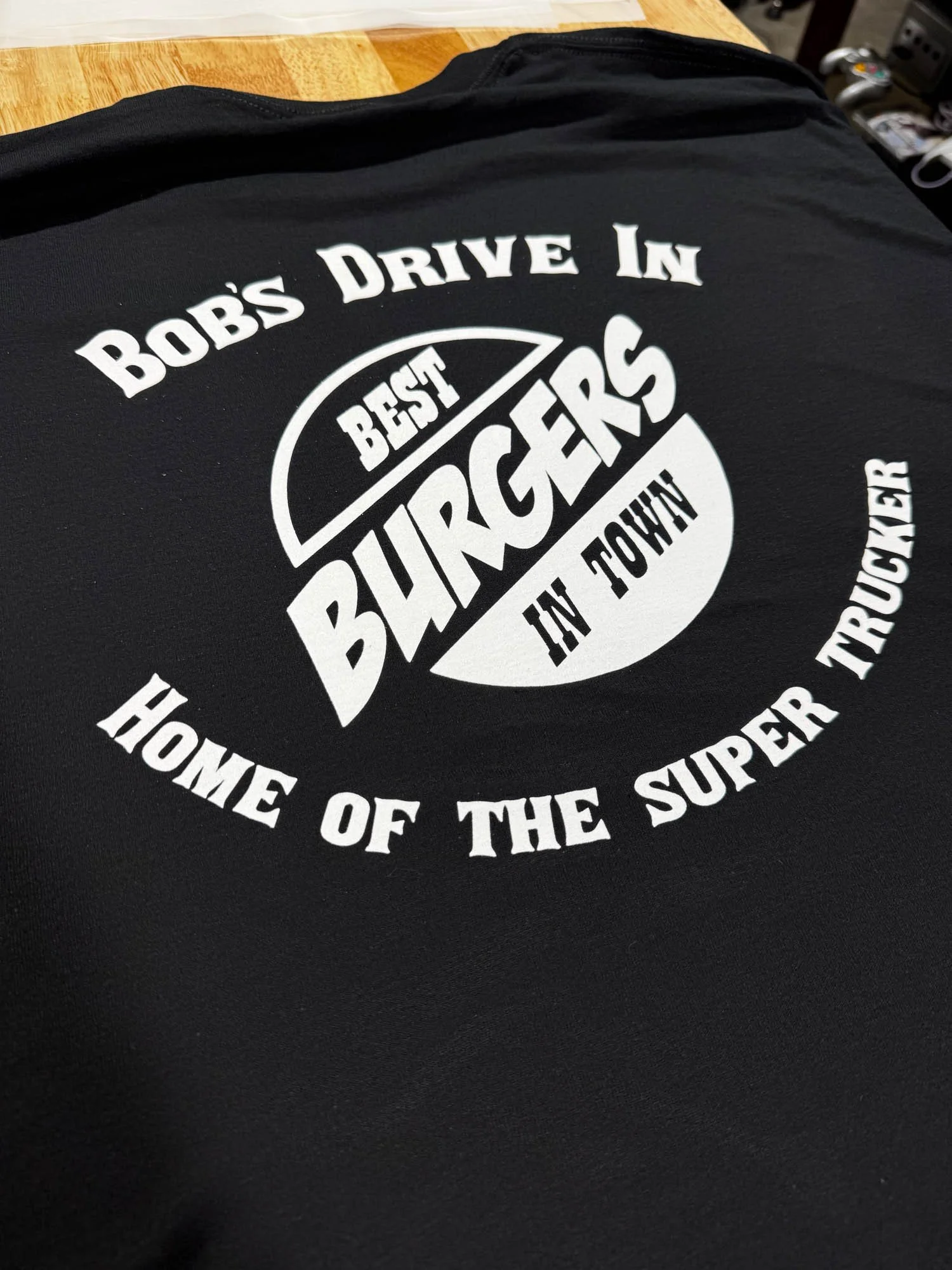 Black T-shirt with white text and graphic design that reads 'Bob's Drive In, Best Burgers in Town, Home of the Super Trucker'.
