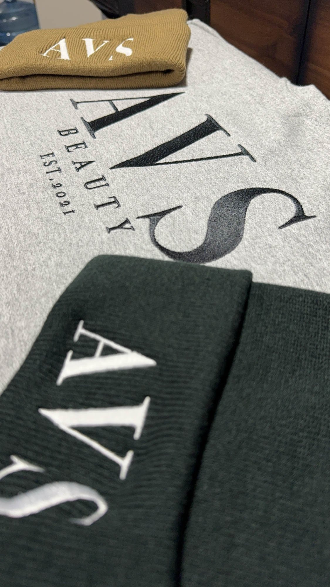 Close-up of fabric swatches with the word 'LUXURY' and 'EST. 1905' printed on a textured fabric surface, with folded cloth pieces in beige, black, and white colors.