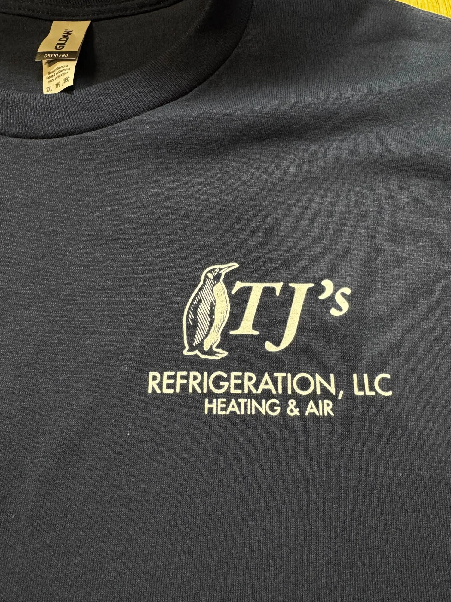 Black T-shirt with logo of a penguin and text that reads 'TJ's Refrigeration, LLC Heating & Air'.