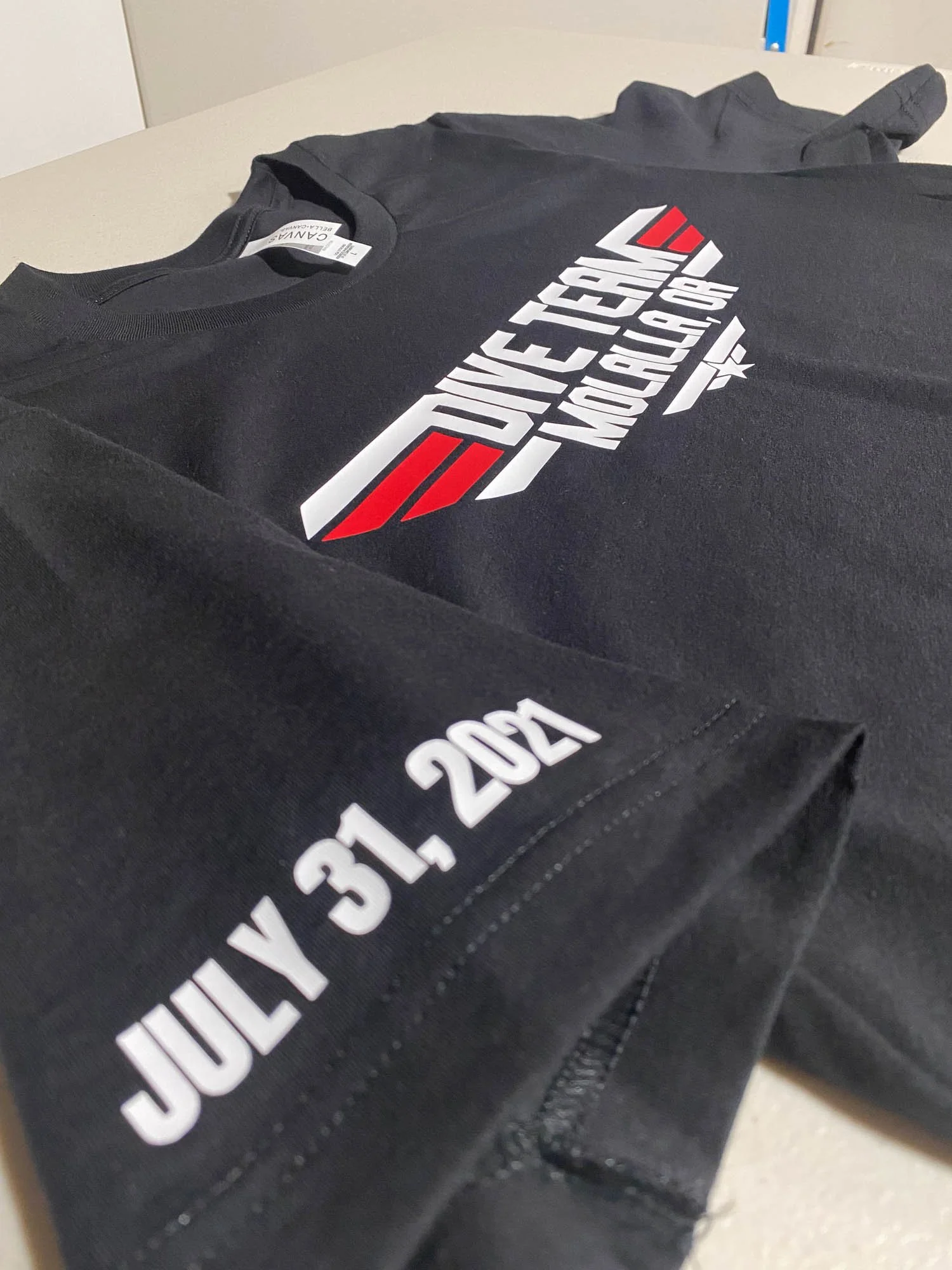 Black T-shirt with a racing event logo and the date July 31, 2021, on the sleeve, laid out on a flat surface.