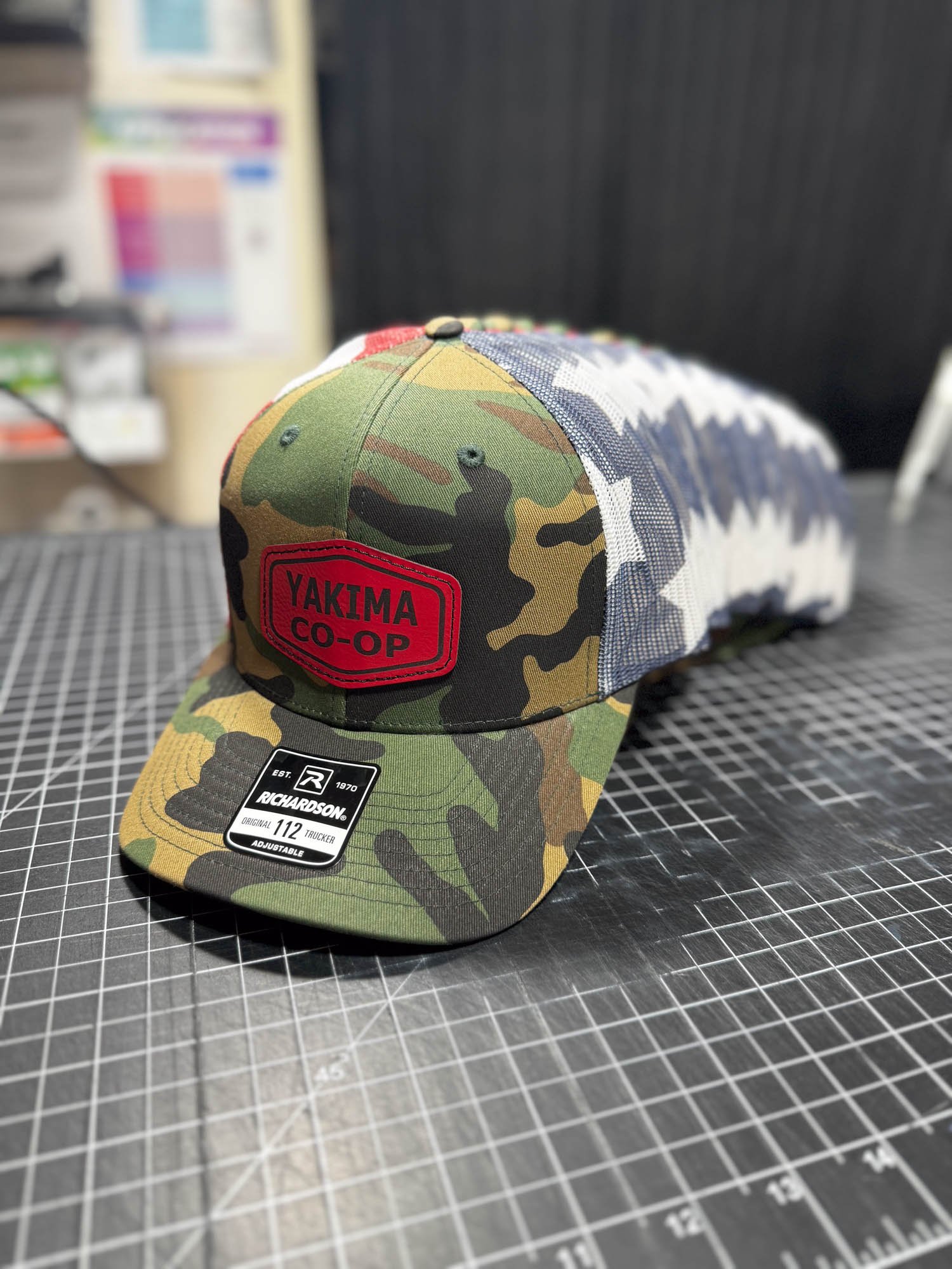 Camouflage baseball cap with a red patch that says 'YAKIMA CO-OP' on the front and a sticker on the brim that reads 'Richardson 112 adjustable'.