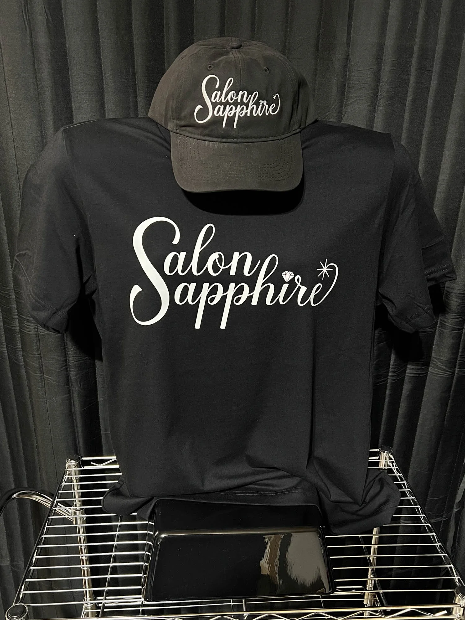 Black t-shirt and cap both with the words "Salon Sapphire" printed in white.