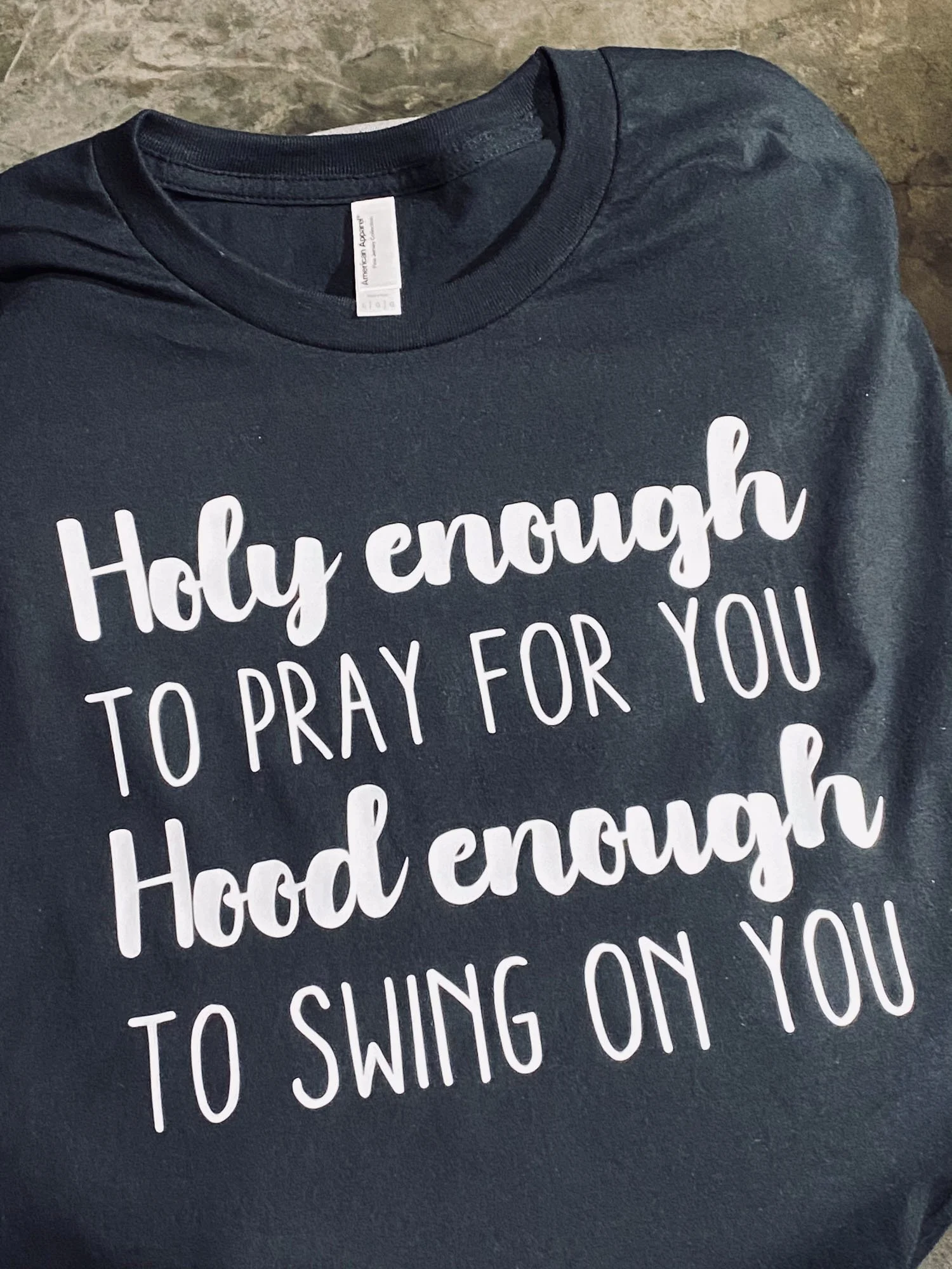 Black T-shirt with white text that reads, "Holy enough to pray for you, Hood enough to swing on you."