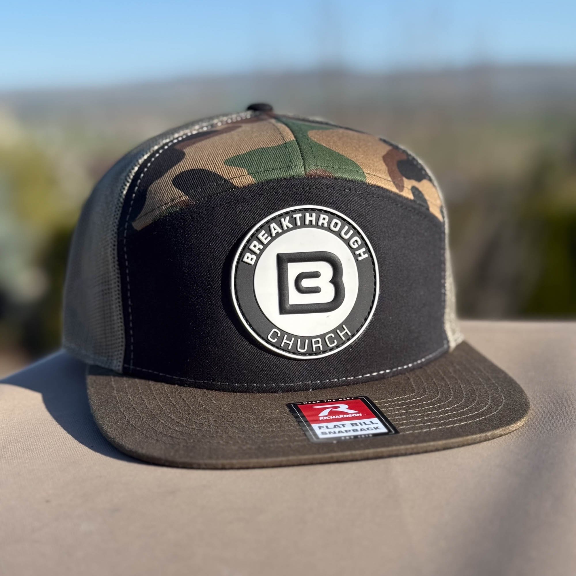 A black, gray, and camouflage trucker cap with a circular patch that says 'Breakthrough Church' and a stylized 'B' inside. The cap has a flat brim and a patch from Richardson brand.