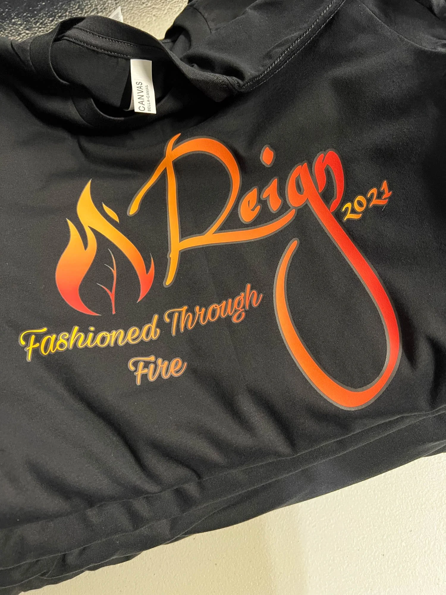 Black jacket with a logo and text in red, orange, and yellow reading 'Design 2021,’ 'Fashioned Through Fire,' and a flame graphic.