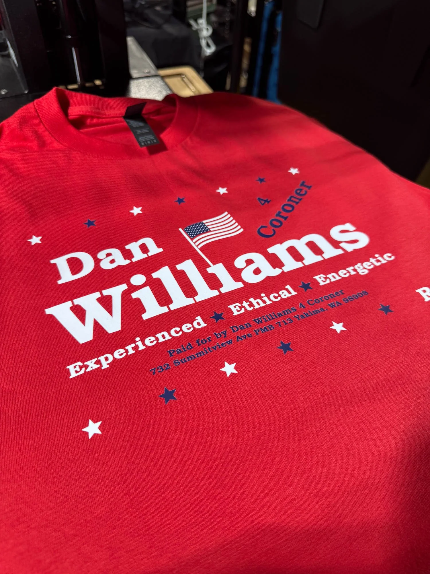 Red T-shirt with campaign-style design for Dan Williams, featuring American flag, stars, and text emphasizing experience, ethics, and energy, with a campaign address.