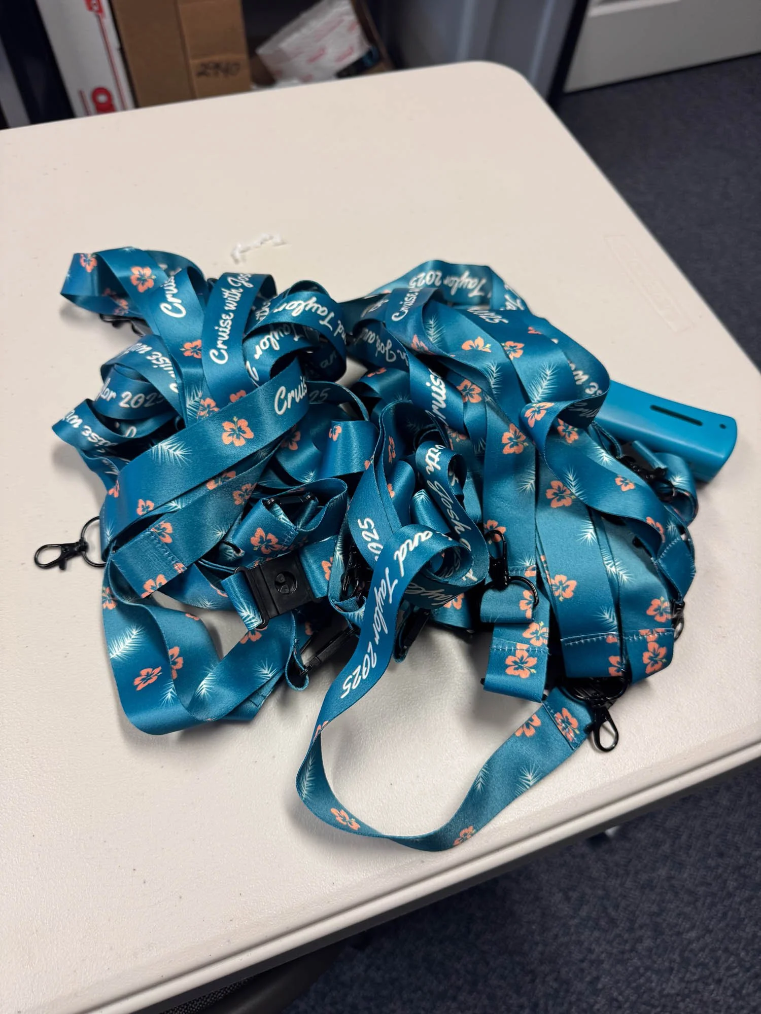 A pile of blue lanyards with orange flowers and white text on a white table.