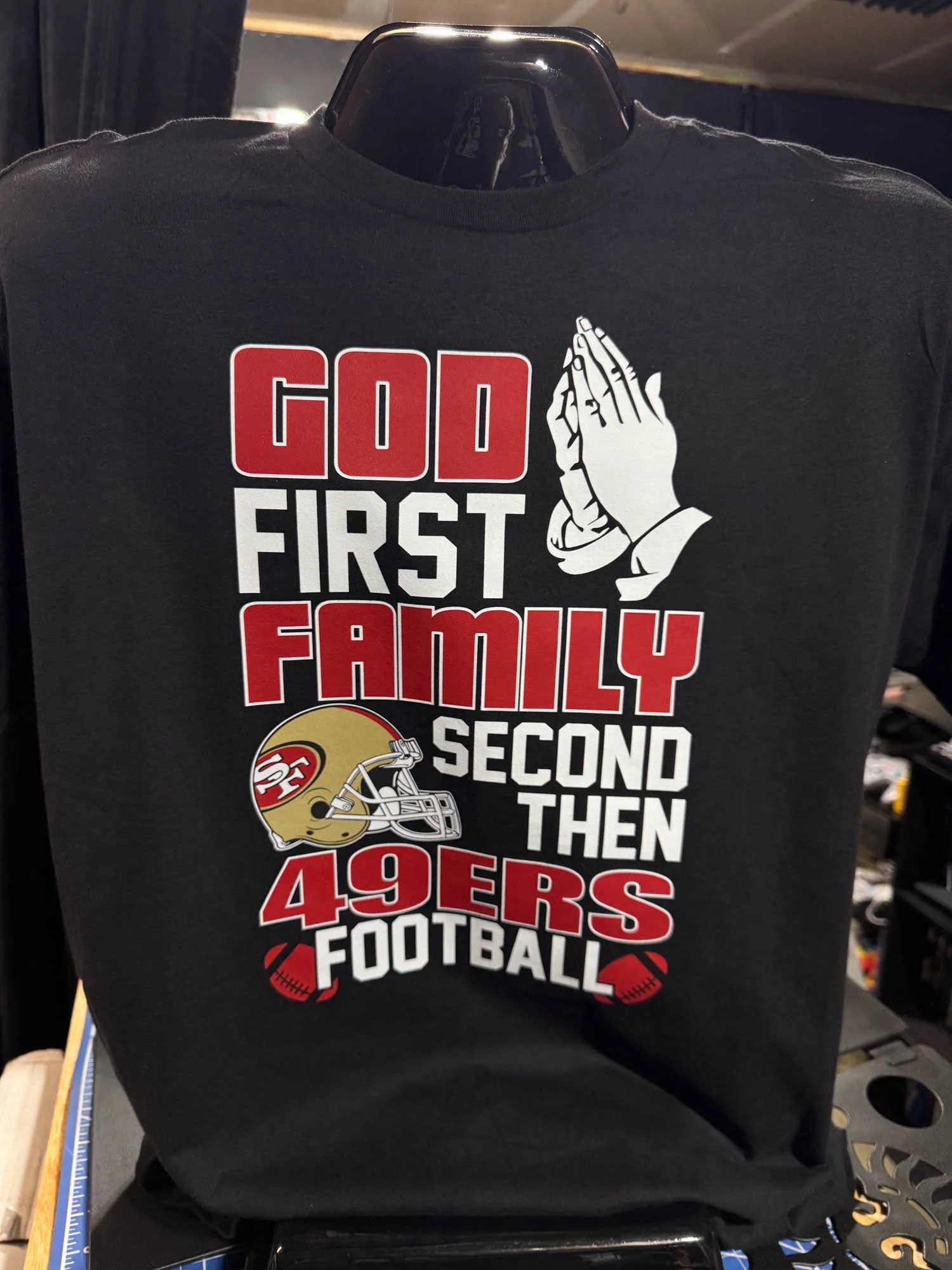 Black T-shirt with the text 'God First Family Second Then 49ers Football', a praying hands graphic, and a San Francisco 49ers helmet graphic.