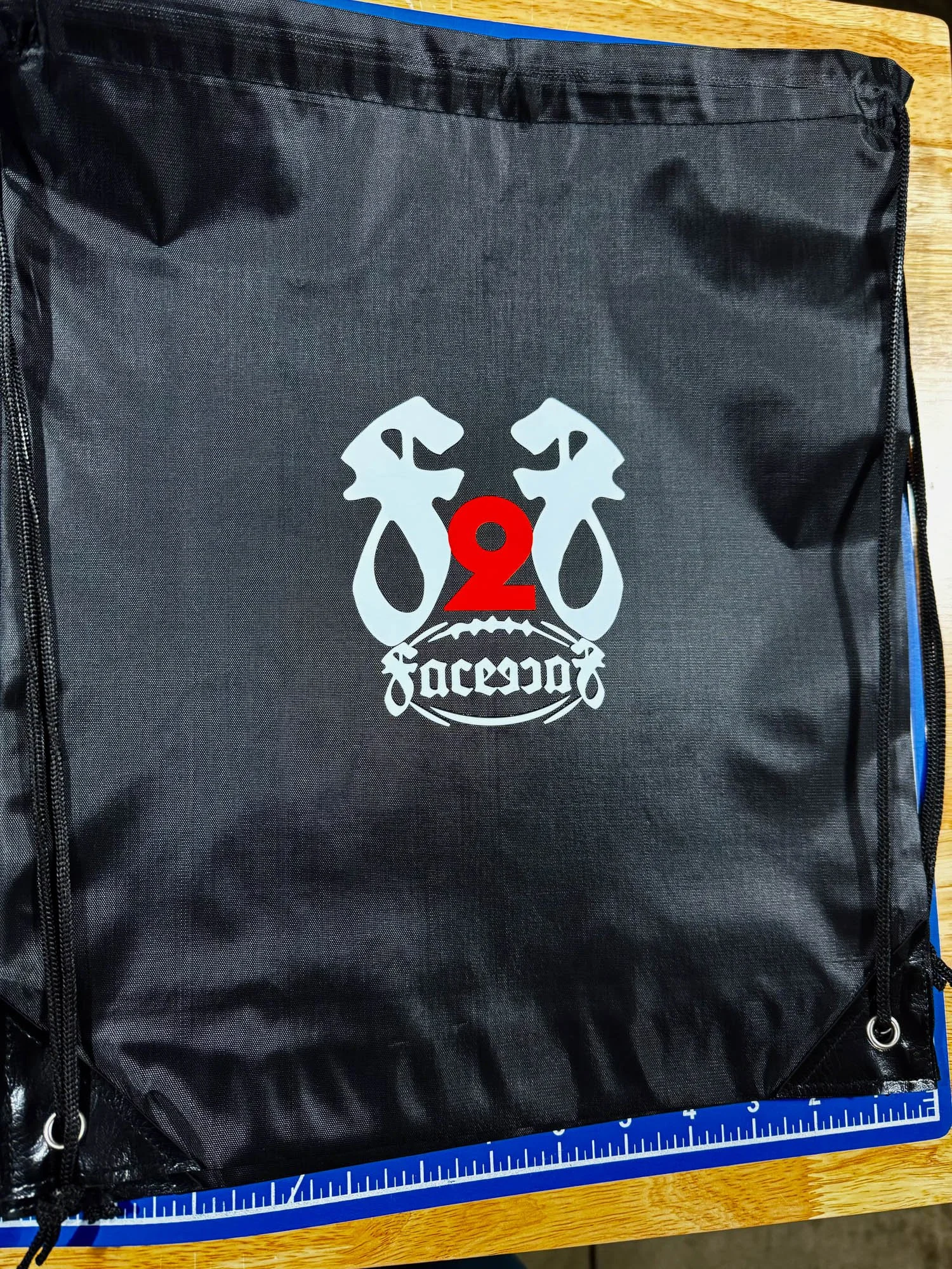 Black drawstring bag with a logo of two stylized lions facing each other, a red number 2 in between, and the word 'Jaceano' beneath.