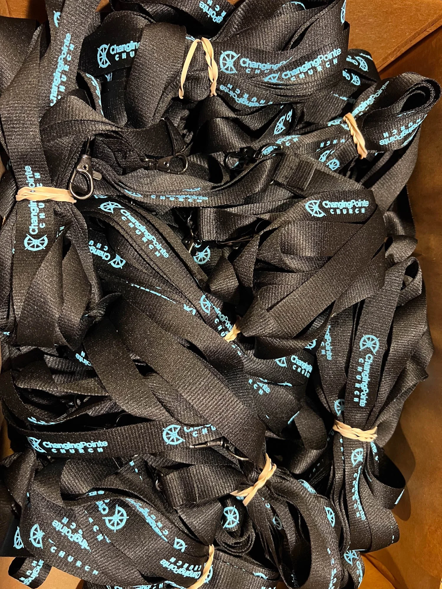 A pile of black lanyards with blue text and logo for Changing Pointe Church, some tied with rubber bands and some with metal clips.