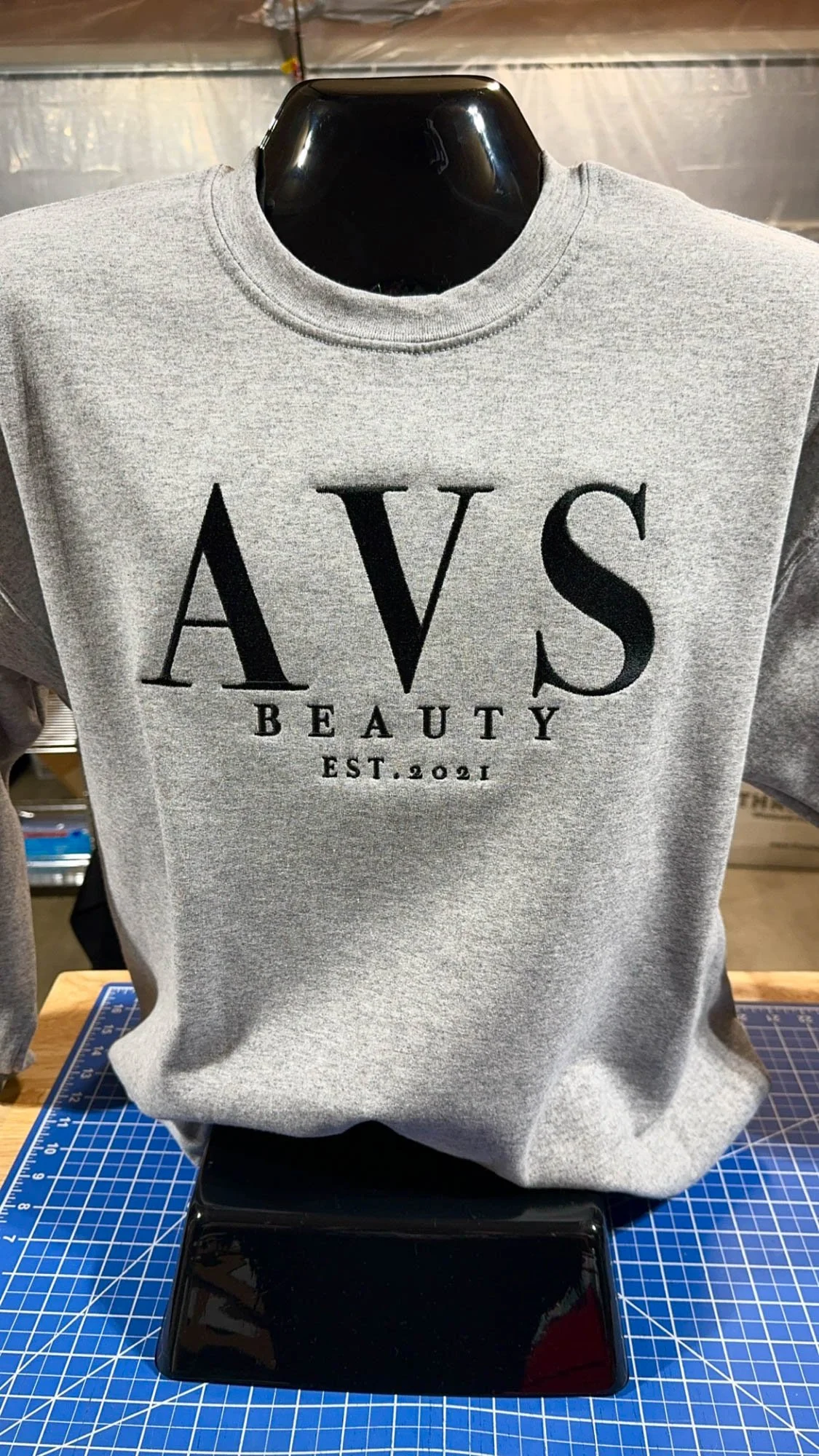 Gray sweatshirt on a mannequin with black text reading 'AVS Beauty Est. 2021'.