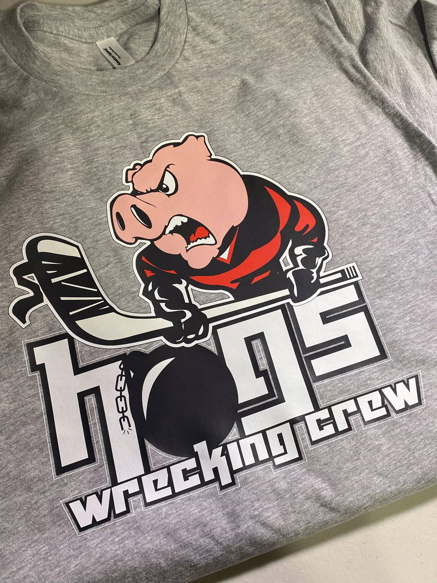 Gray T-shirt with a cartoon pig holding a hockey stick and a black wrecking ball, with the words "Wrecking Crew".