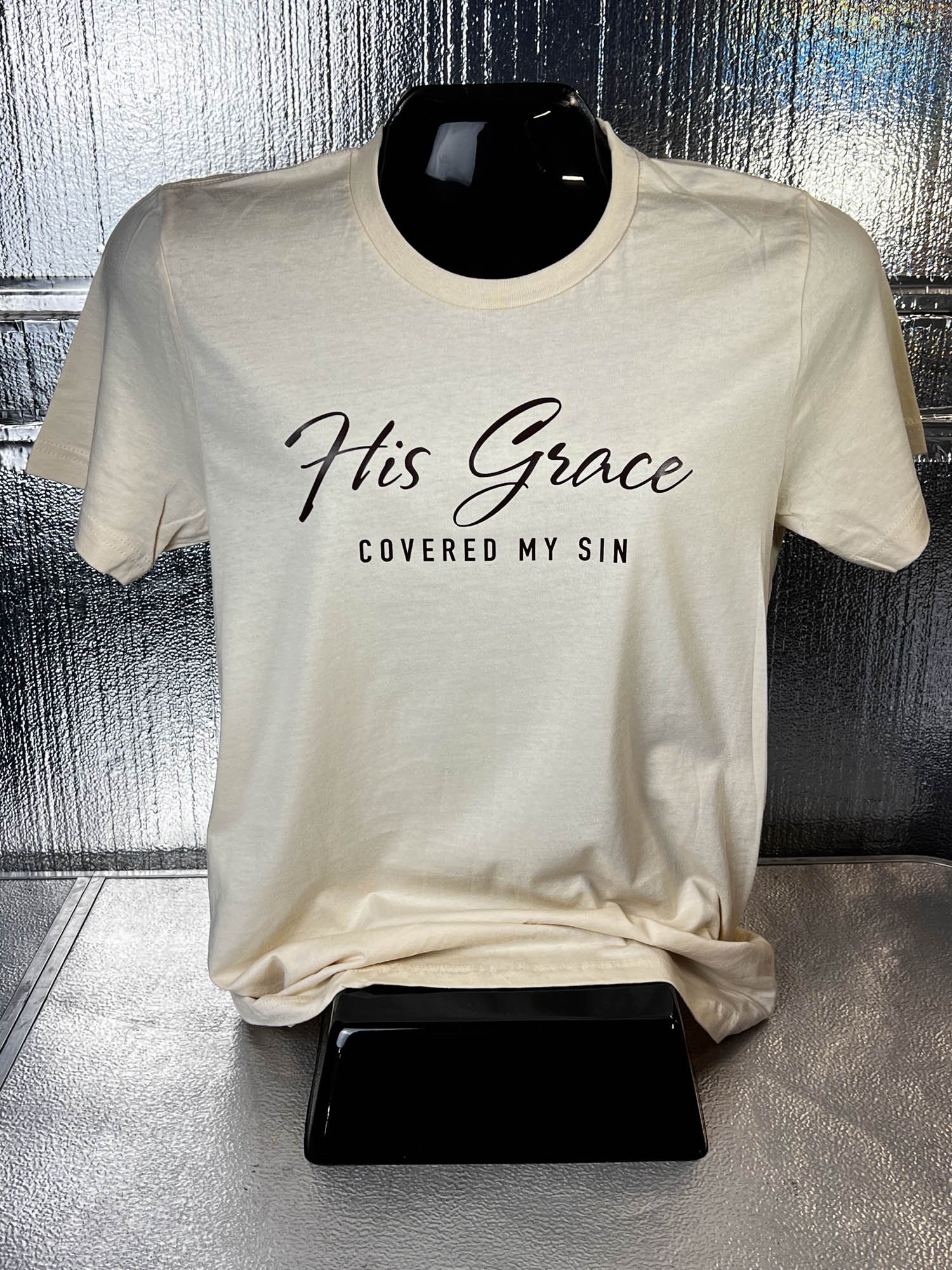 A white T-shirt displayed on a black mannequin, with the text 'His Grace Covered My Sin' printed on the front.