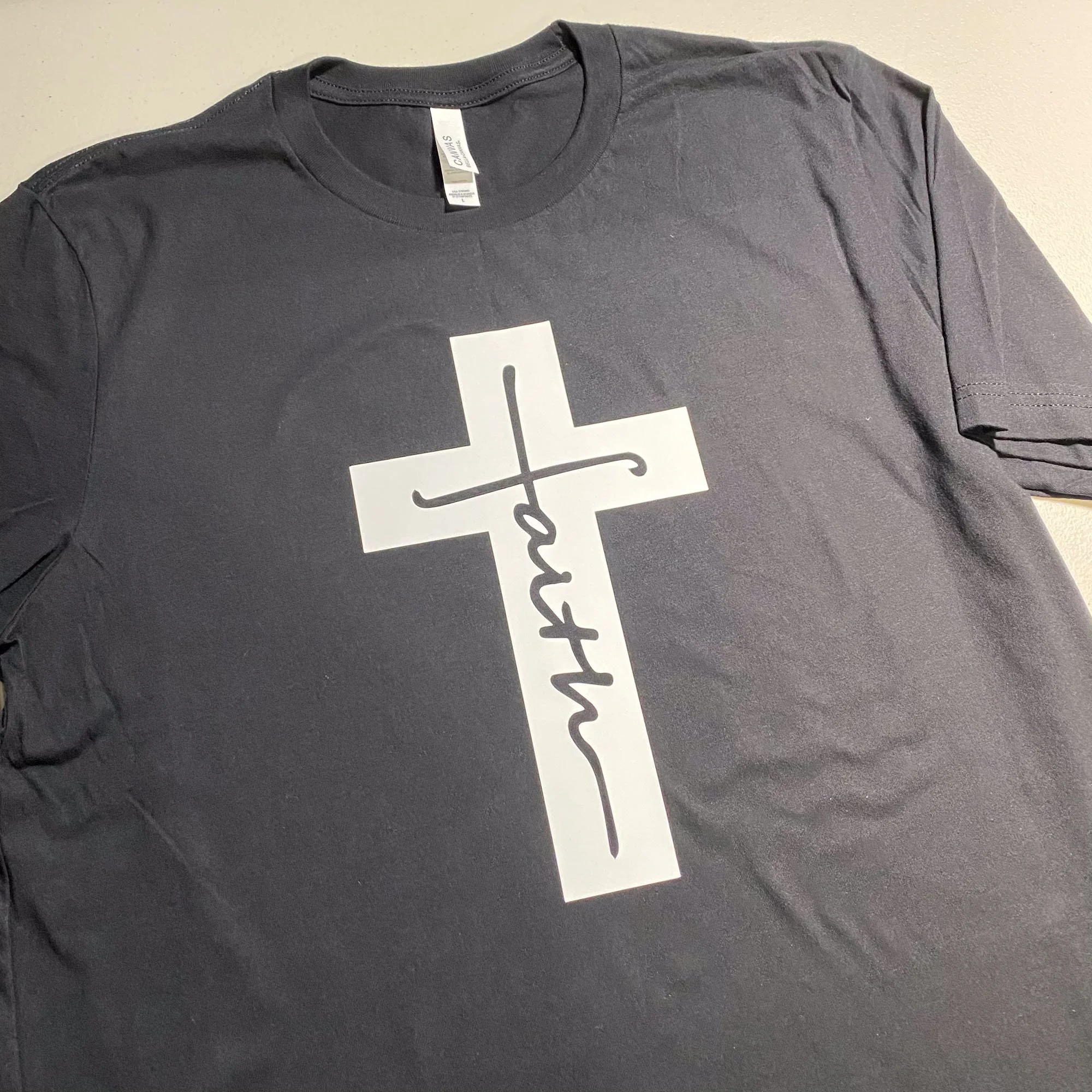Gray t-shirt with a white cross and the word 'faith' written vertically in cursive inside the cross.