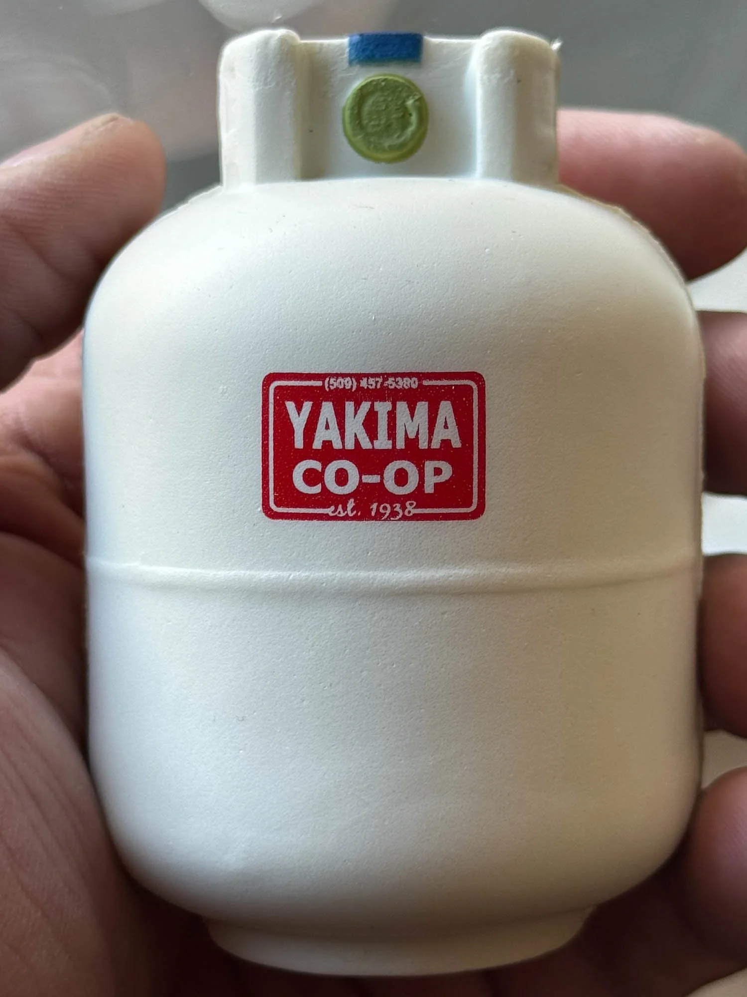 A miniature replica of a vintage white thermos with a green and blue detail at the top, bearing a red and white logo that reads "YAKIMA CO-OP est. 1938".