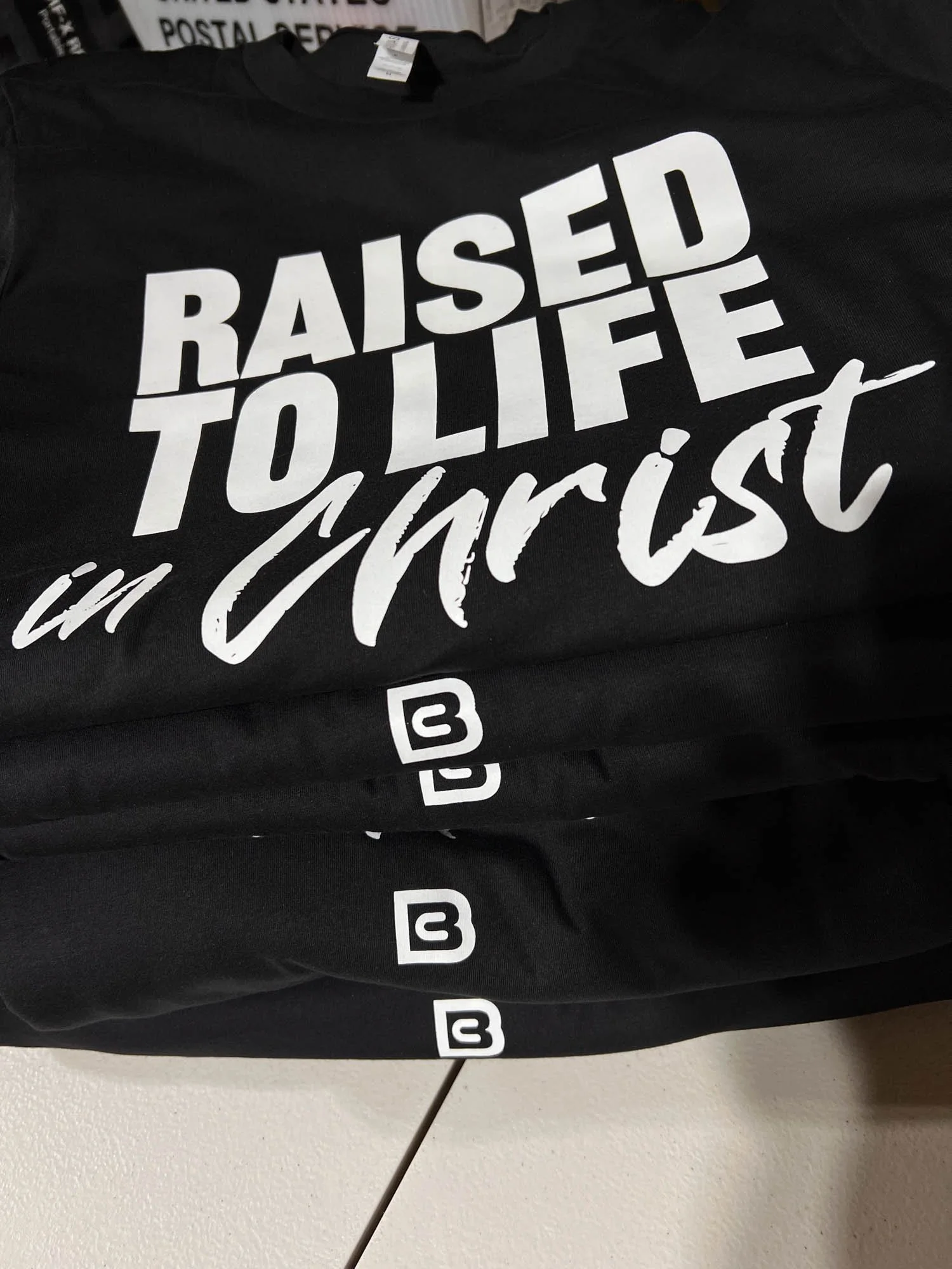 Black T-shirt with white text that reads, "RAISED TO LIVE in Christ" and social media icons.