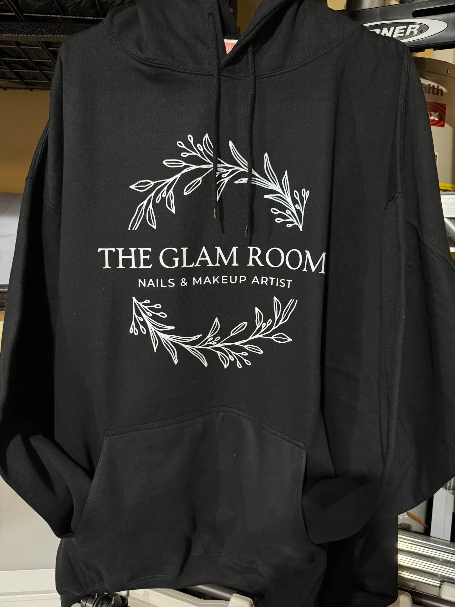 Black hoodie with white text and botanical illustrations reading 'The Glam Room Nails & Makeup Artist' on the front.