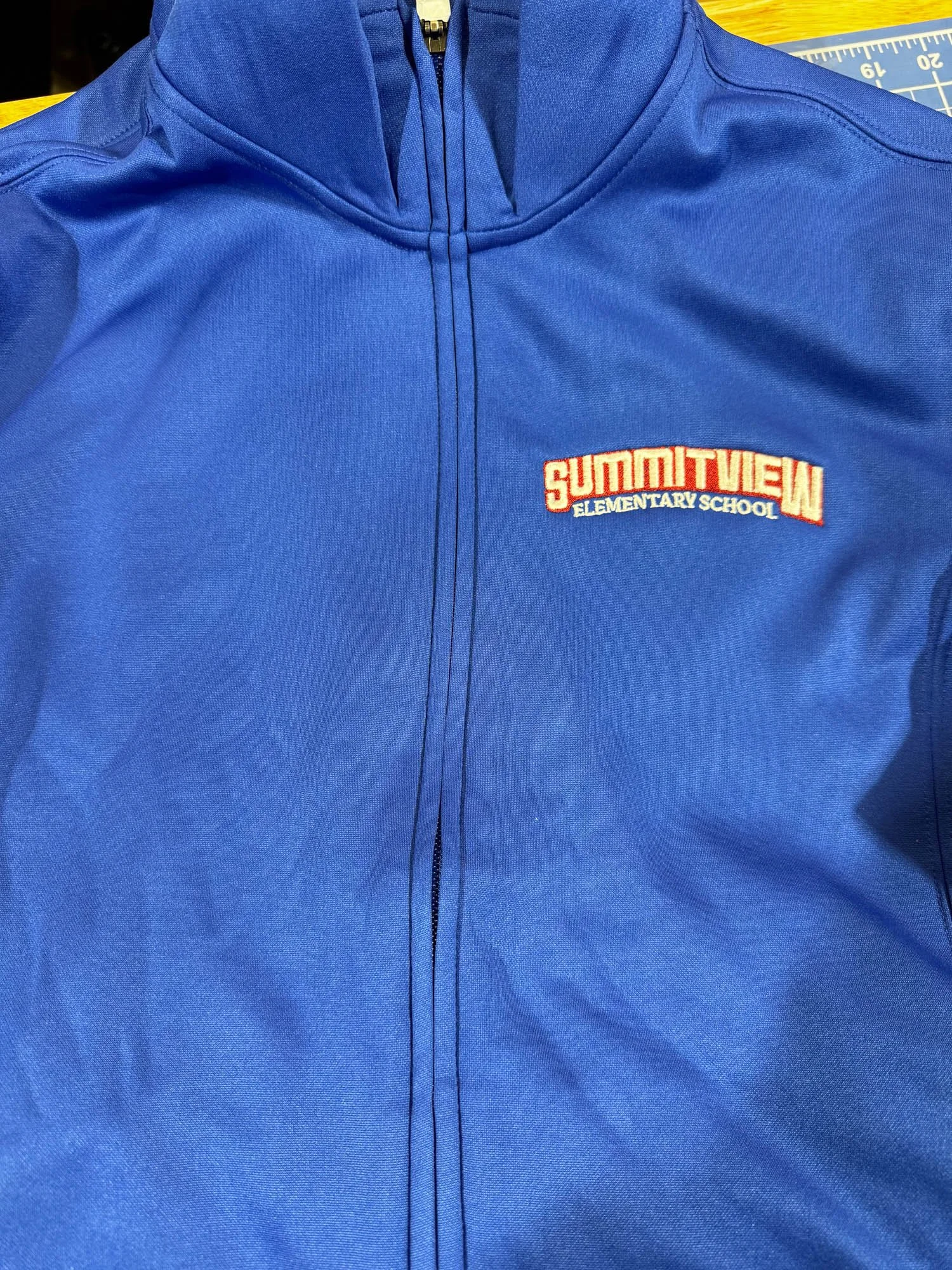 A blue zip-up jacket with an embroidered patch on the chest reading "SUMMITVIEW ELEMENTARY SCHOOL" in red and white text.