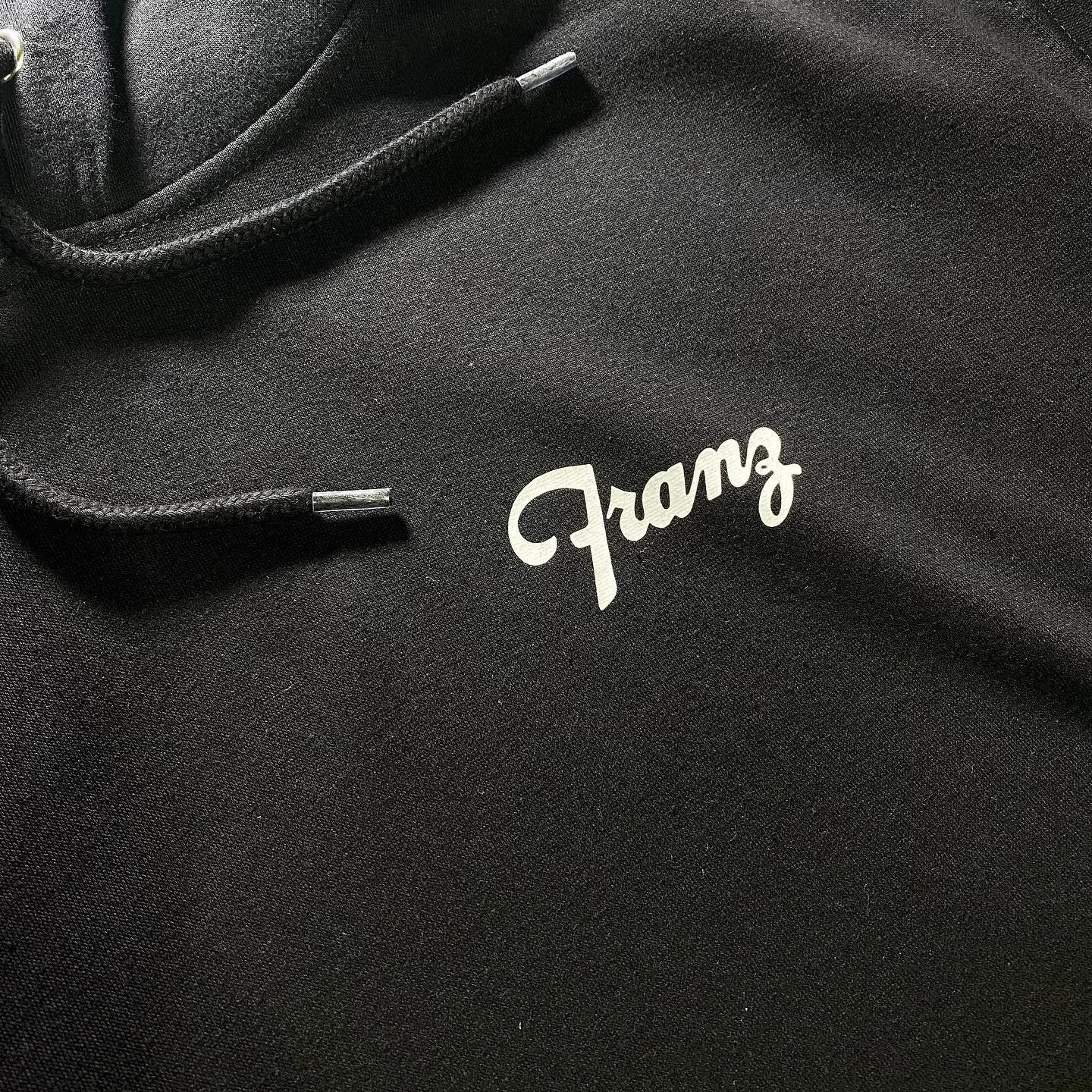 Close-up of a black fabric surface with a white 'Famous' logo and black drawstrings with metallic tips.