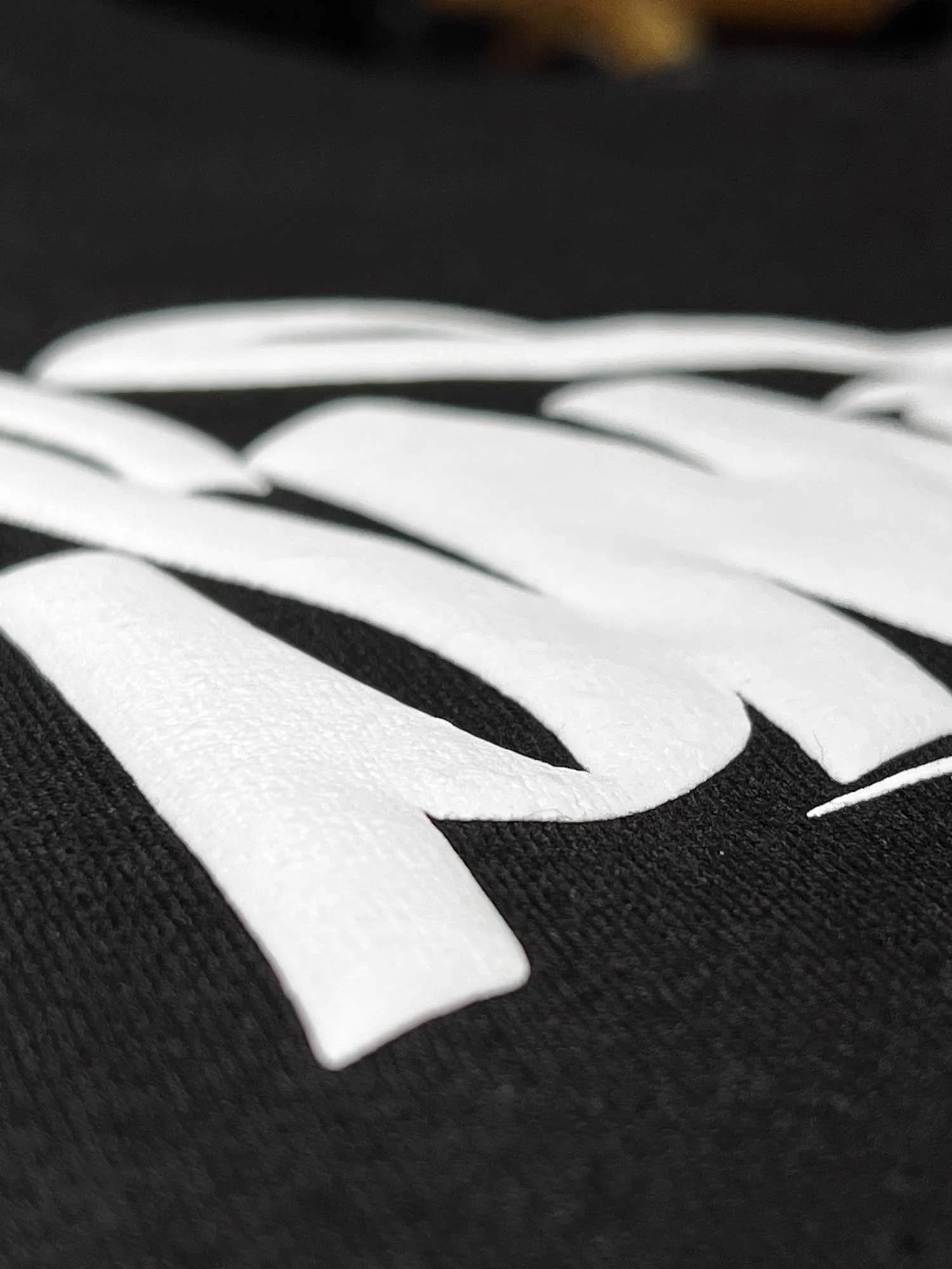 Close-up of white text on black fabric, showing partial word or logo.