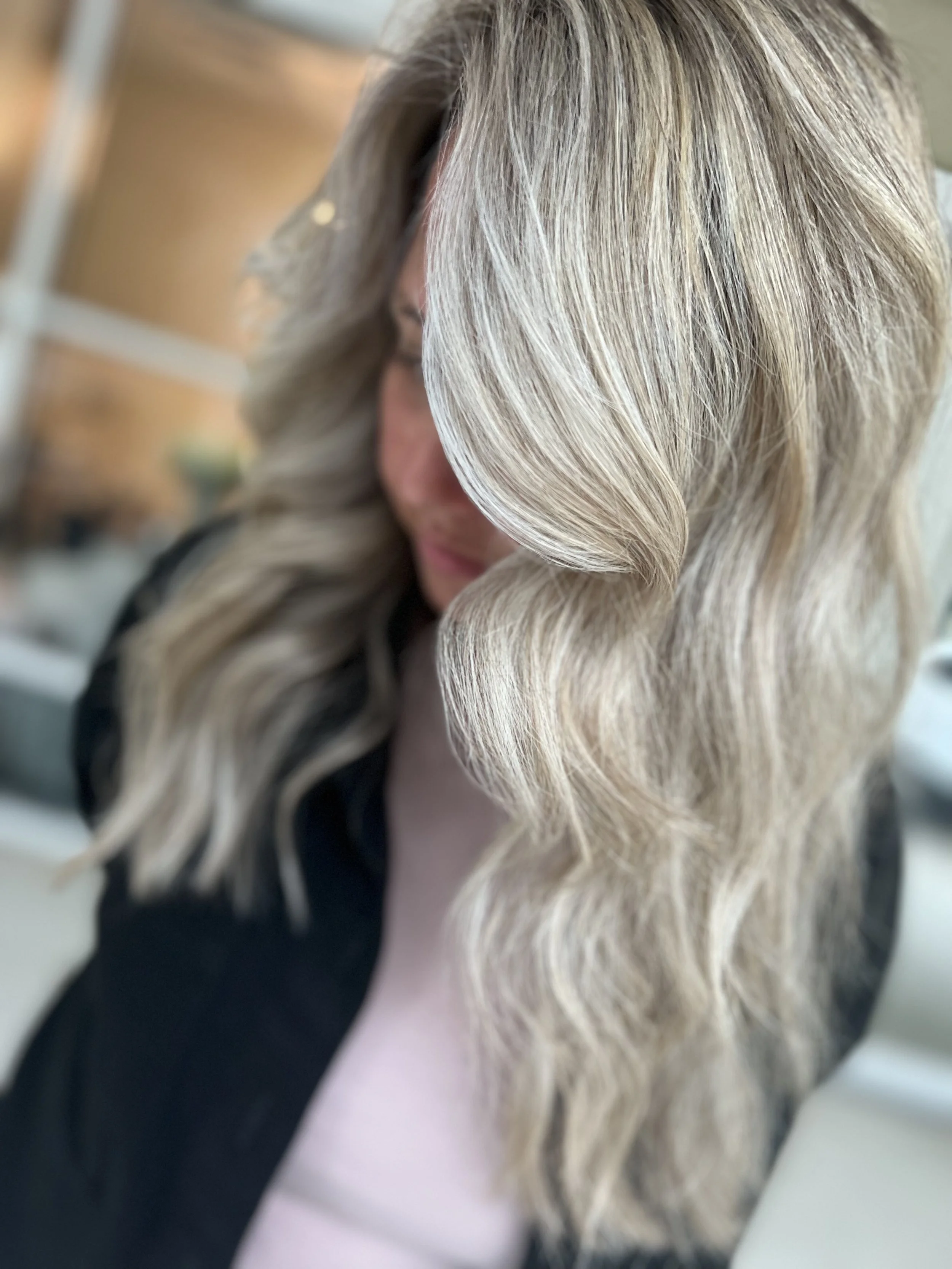 Close-up of a woman with long wavy blonde hair, partially obscuring her face, in an indoor setting.