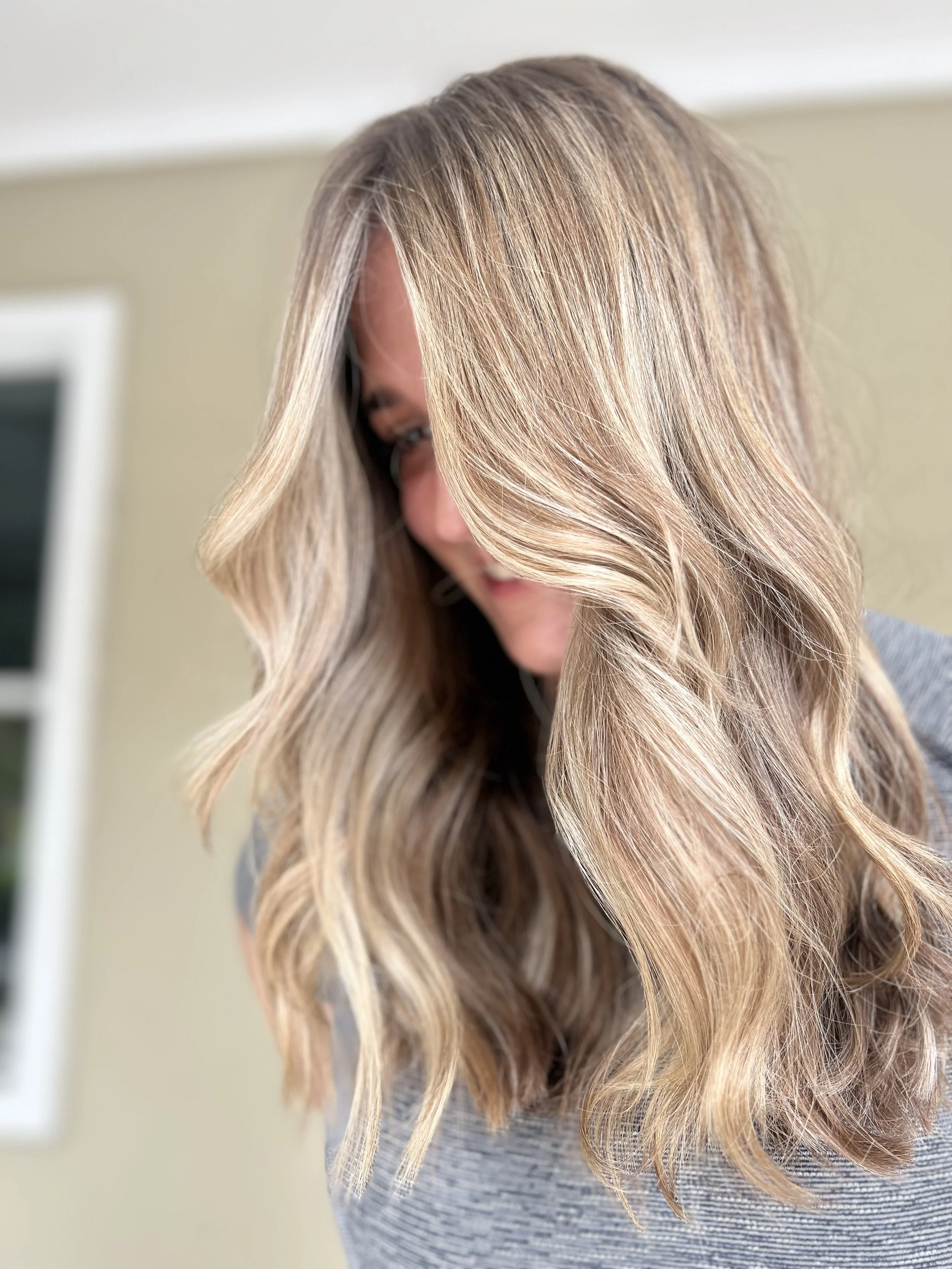A woman with long, wavy blonde hair looking down and smiling.