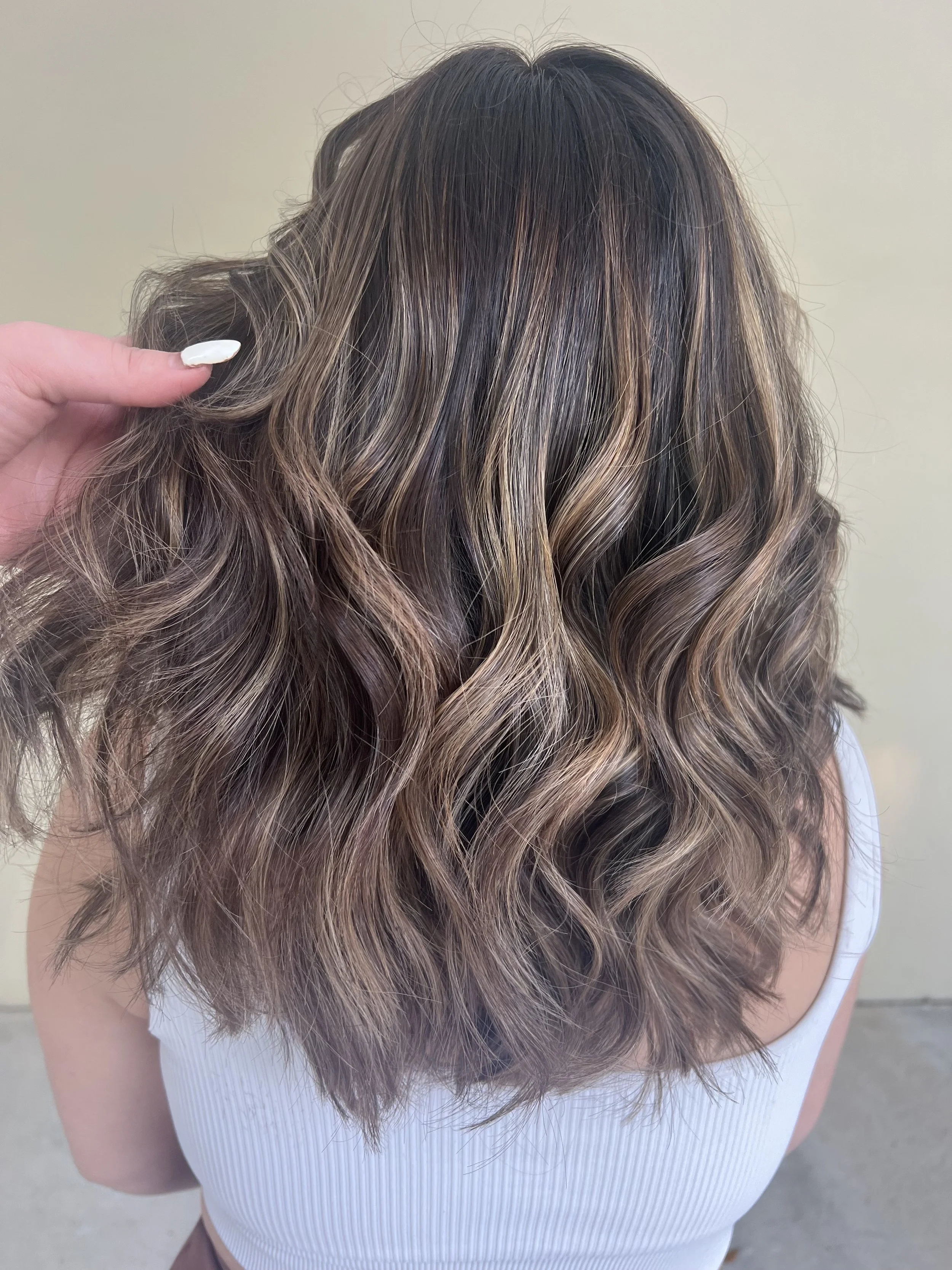 Back view of a woman with shoulder-length, wavy hair with highlights in shades of brown and blonde.
