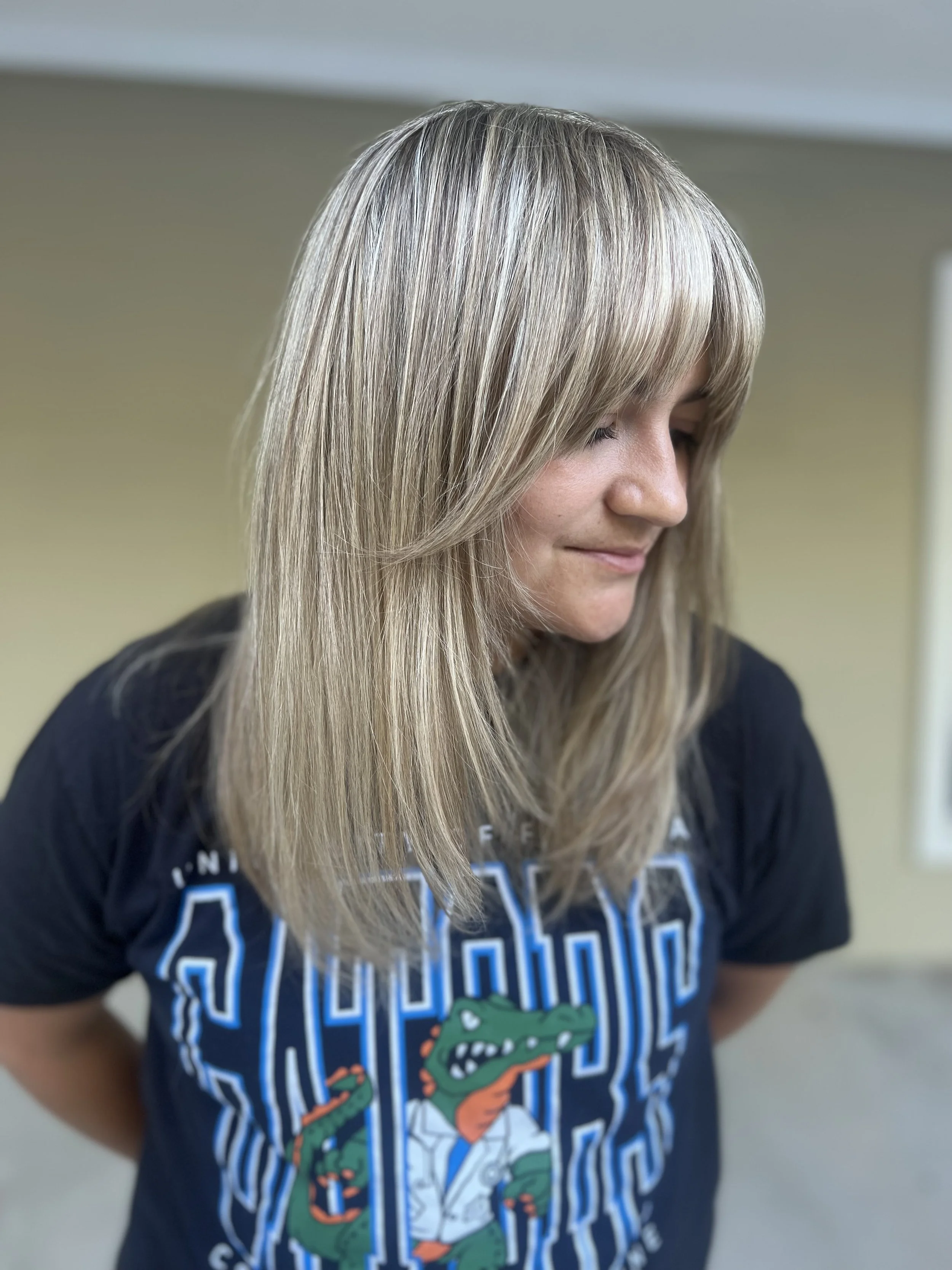 Woman with blonde hair wearing a black T-shirt with an alligator graphic and Vanderbilt logo, looking down.