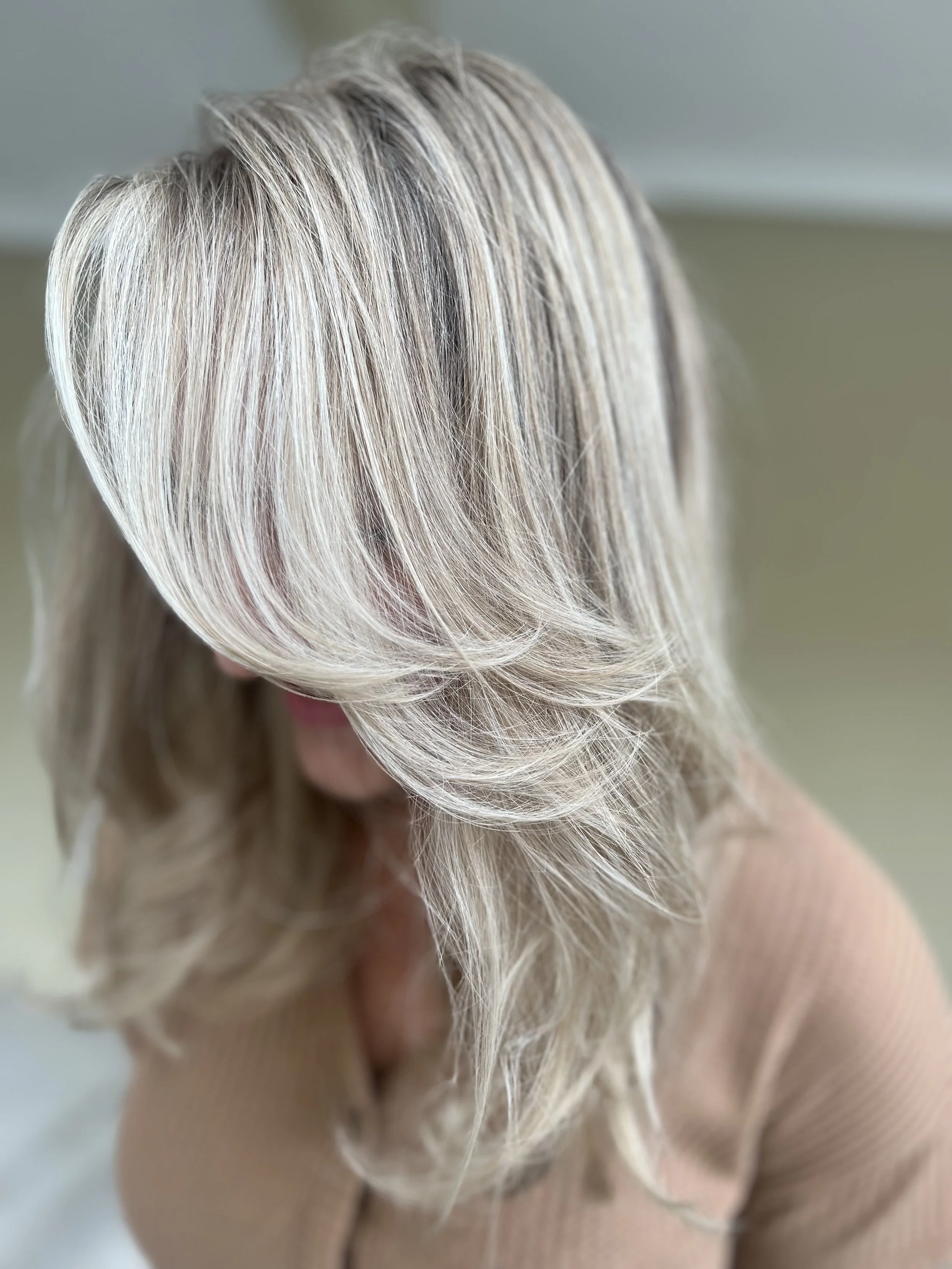 Close-up of a woman with shoulder-length layered blonde hair with highlights, wearing a beige sweater.