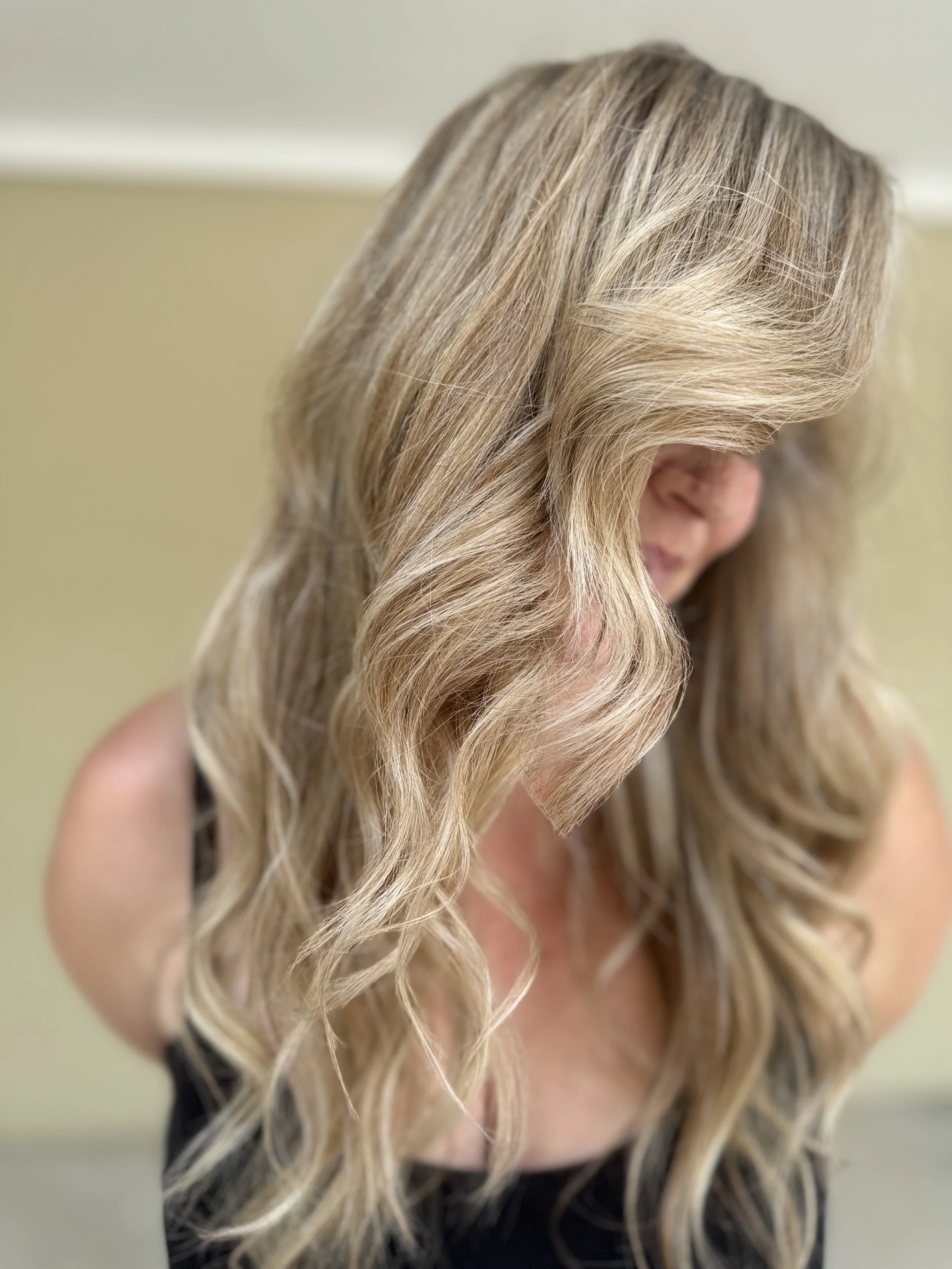 A woman with long, wavy blonde hair looking down, wearing a black top.