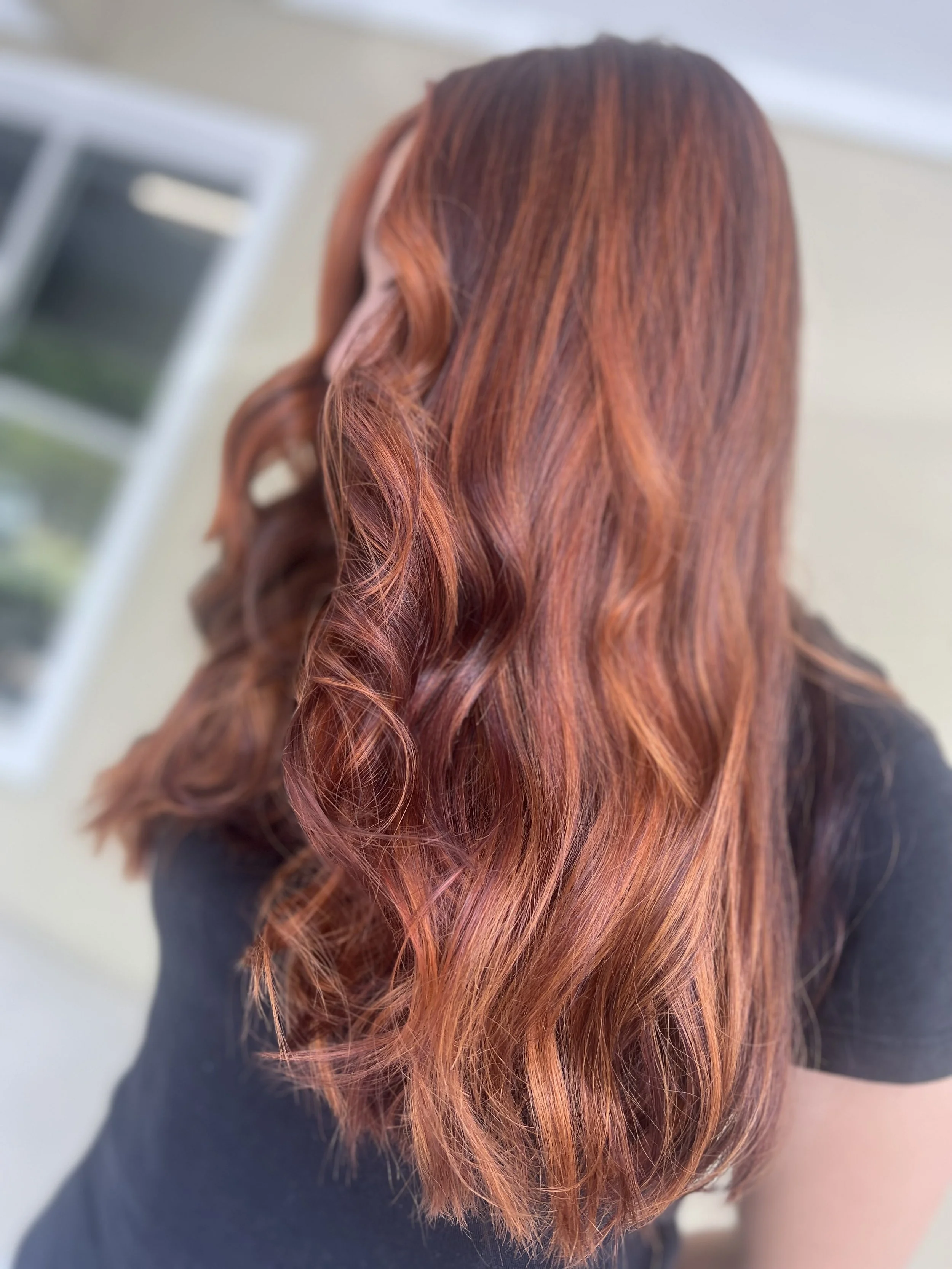 Back view of a woman with long, wavy, reddish-brown hair.