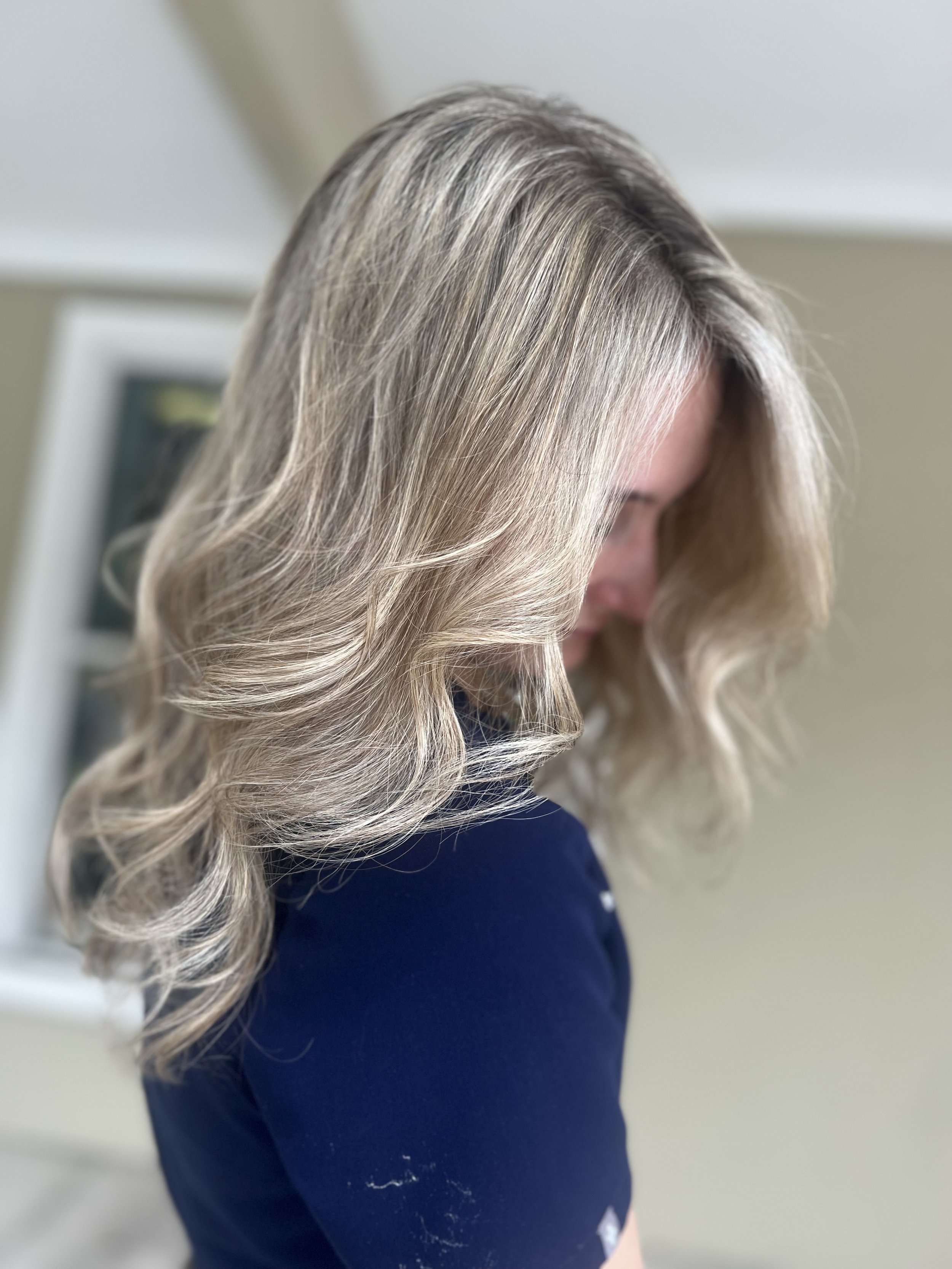 A woman with shoulder-length blonde hair styled in loose waves, wearing a dark blue top.