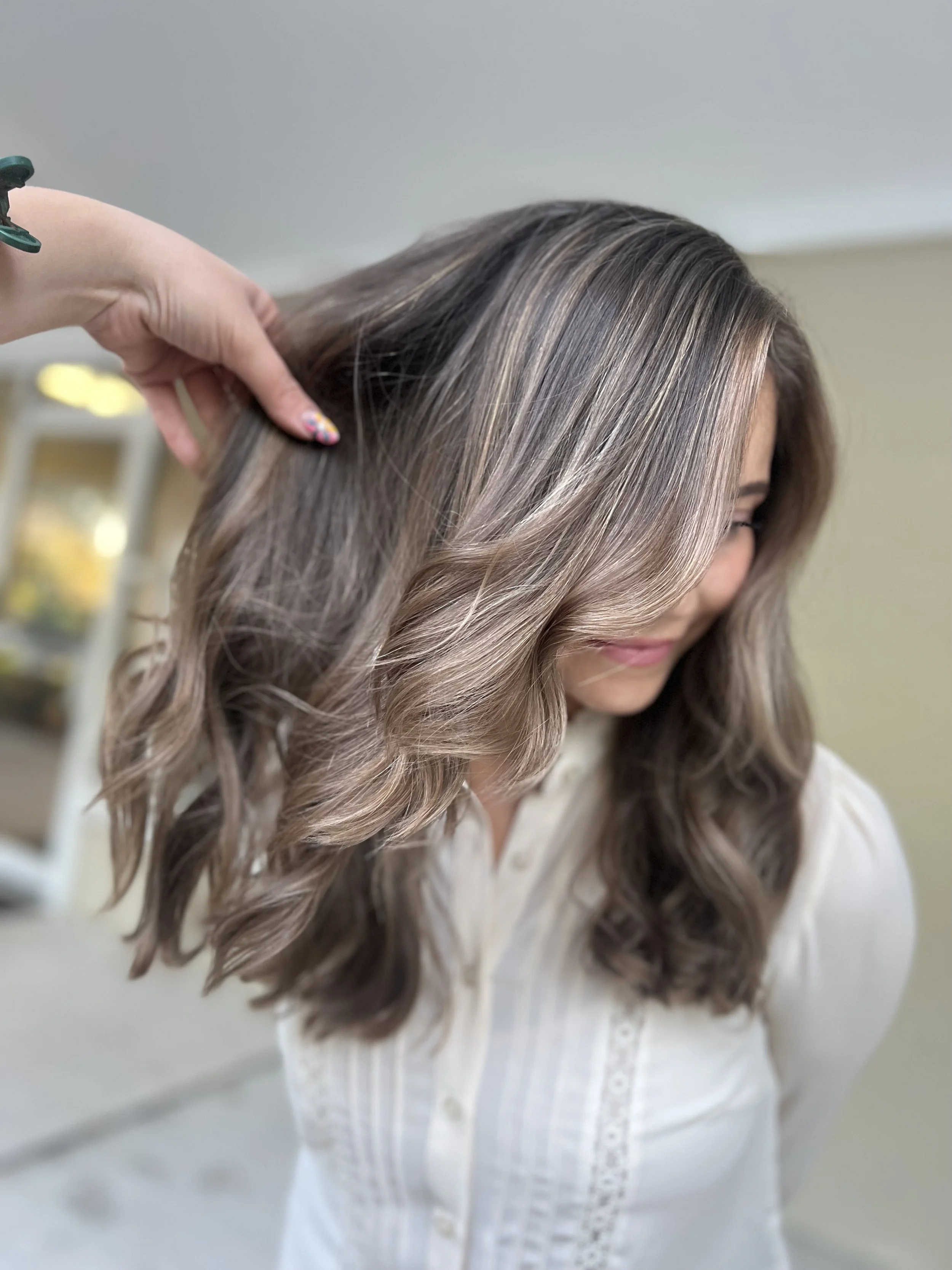 Woman with shoulder-length wavy hair getting her hair styled or highlighted by a professional.