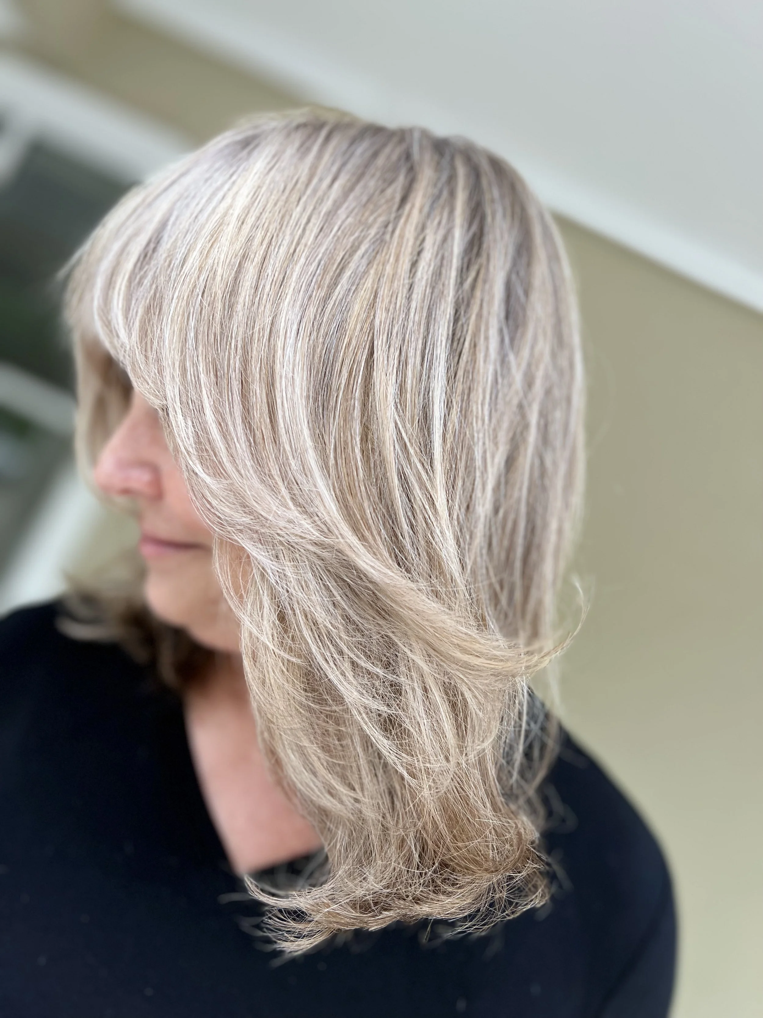 Close-up of a woman with shoulder-length blonde hair styled with loose waves, wearing a black top, with a neutral background.