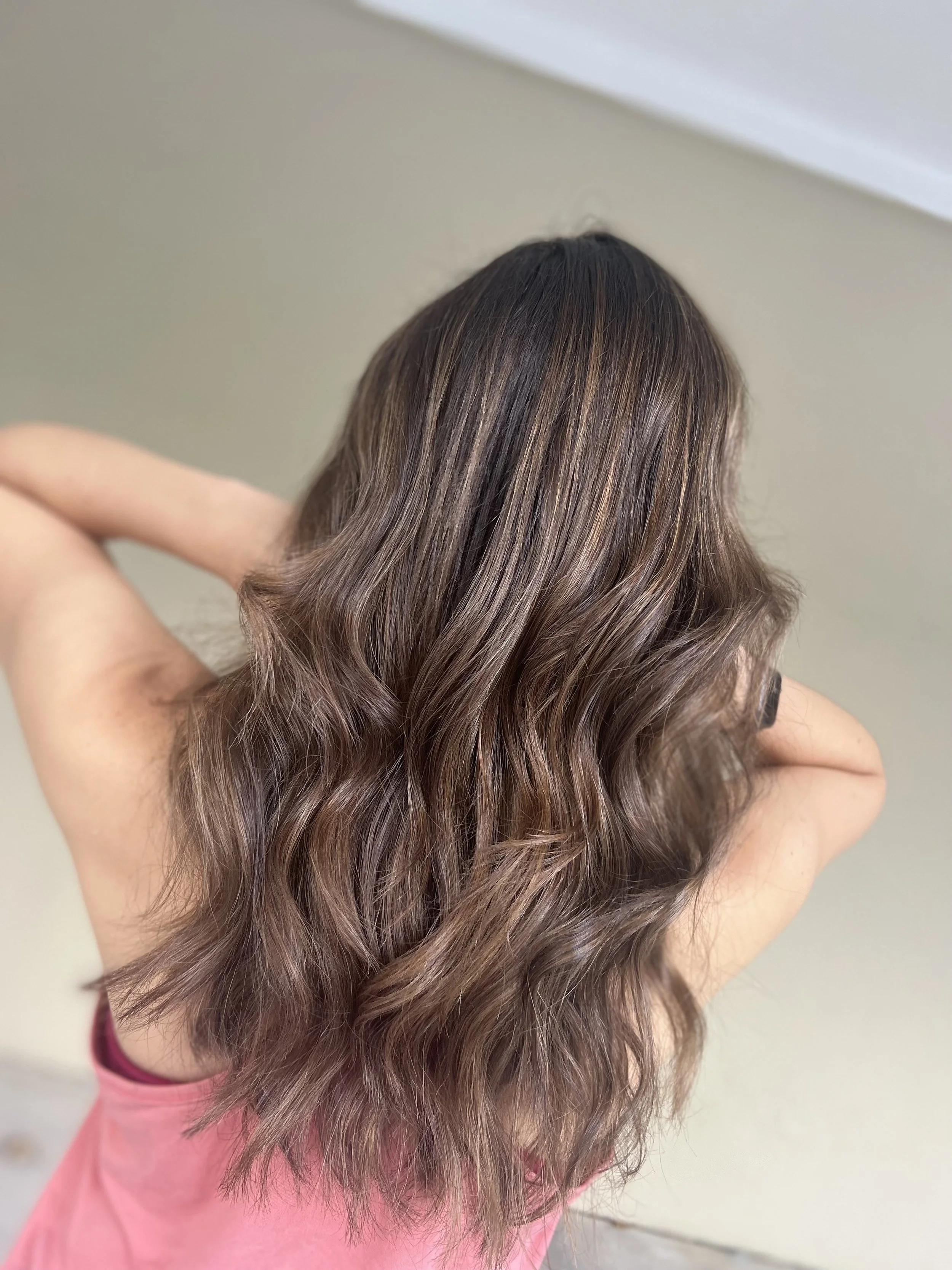 Back view of a woman with shoulder-length wavy brown hair with subtle highlights.