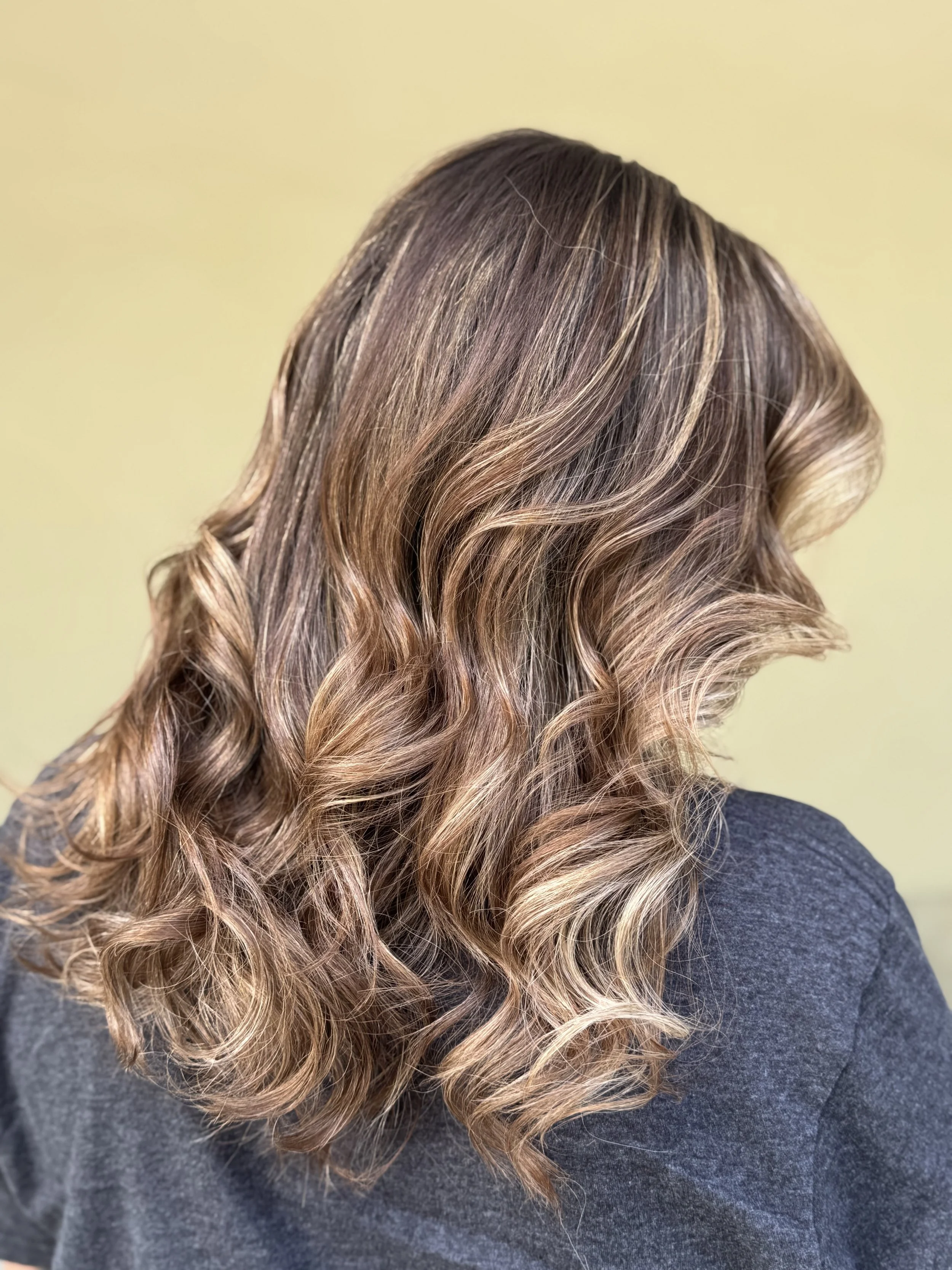 Woman with shoulder-length, wavy, brown hair with blonde highlights wearing a dark gray top