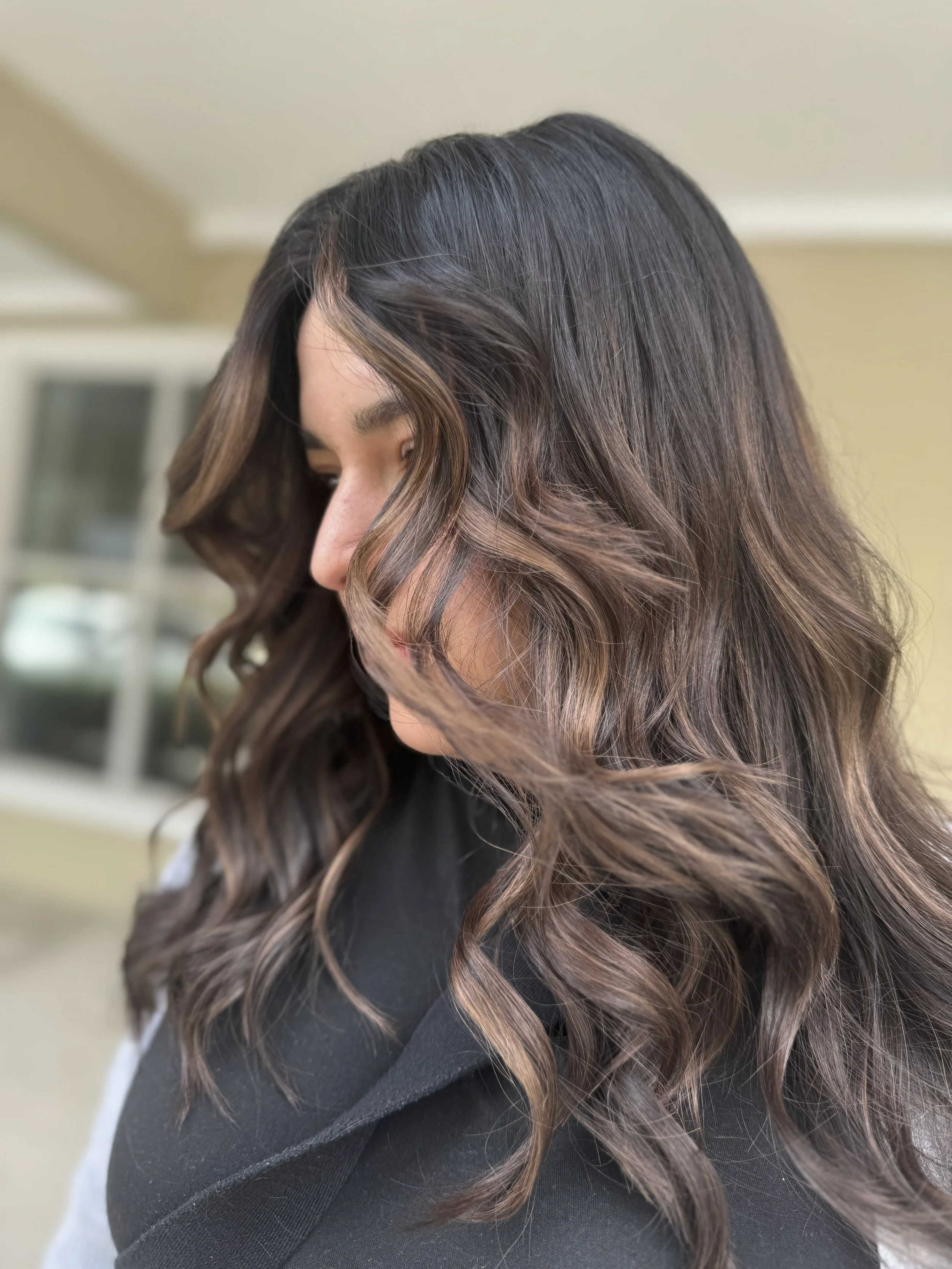 Close-up of a woman with long, wavy brown hair with highlights, looking downward.