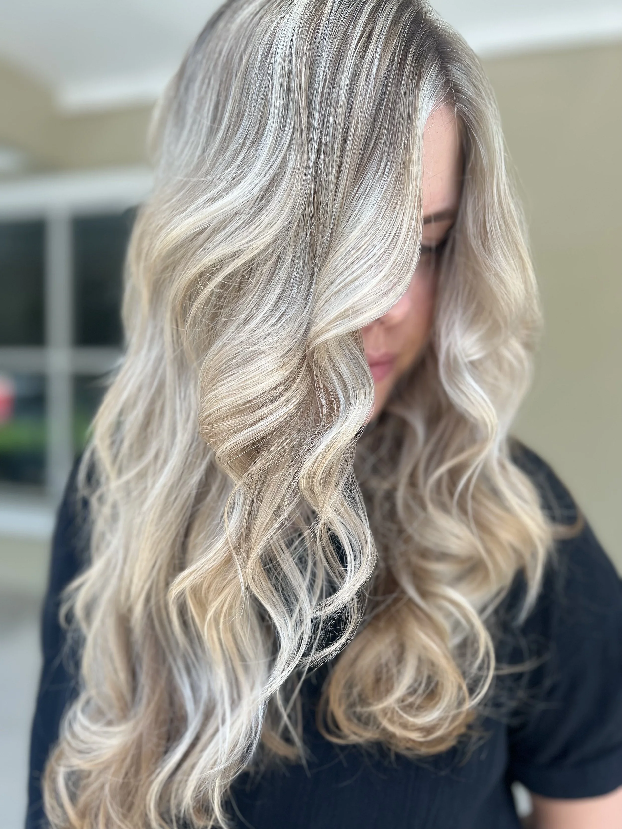 Woman with long, wavy blonde hair with highlights, looking down.