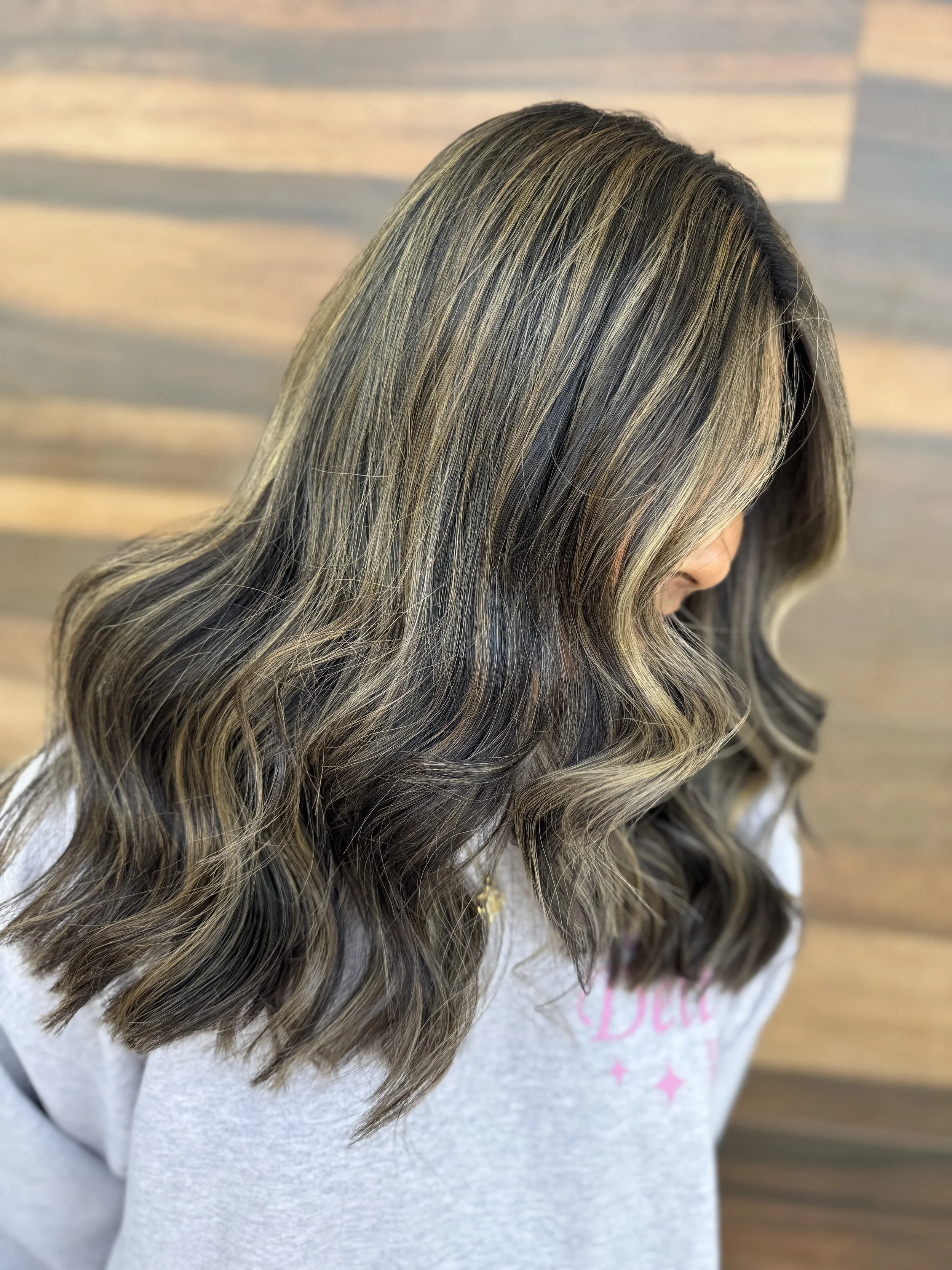 Side view of a woman with wavy hairstyle featuring blonde highlights and darker lowlights.