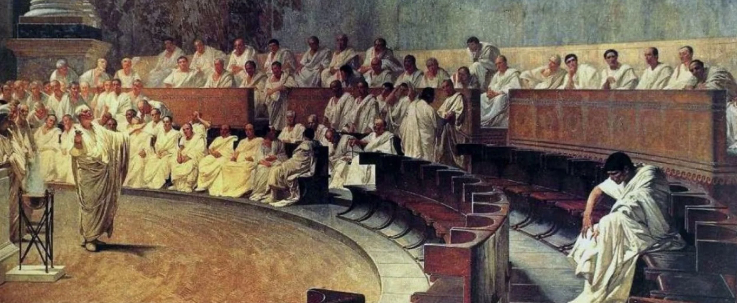 A painting of a large group of Pallavas or scholars in traditional Indian attire sitting and standing in a semi-circular lecture hall or assembly setting, with a man standing and speaking at the front.
