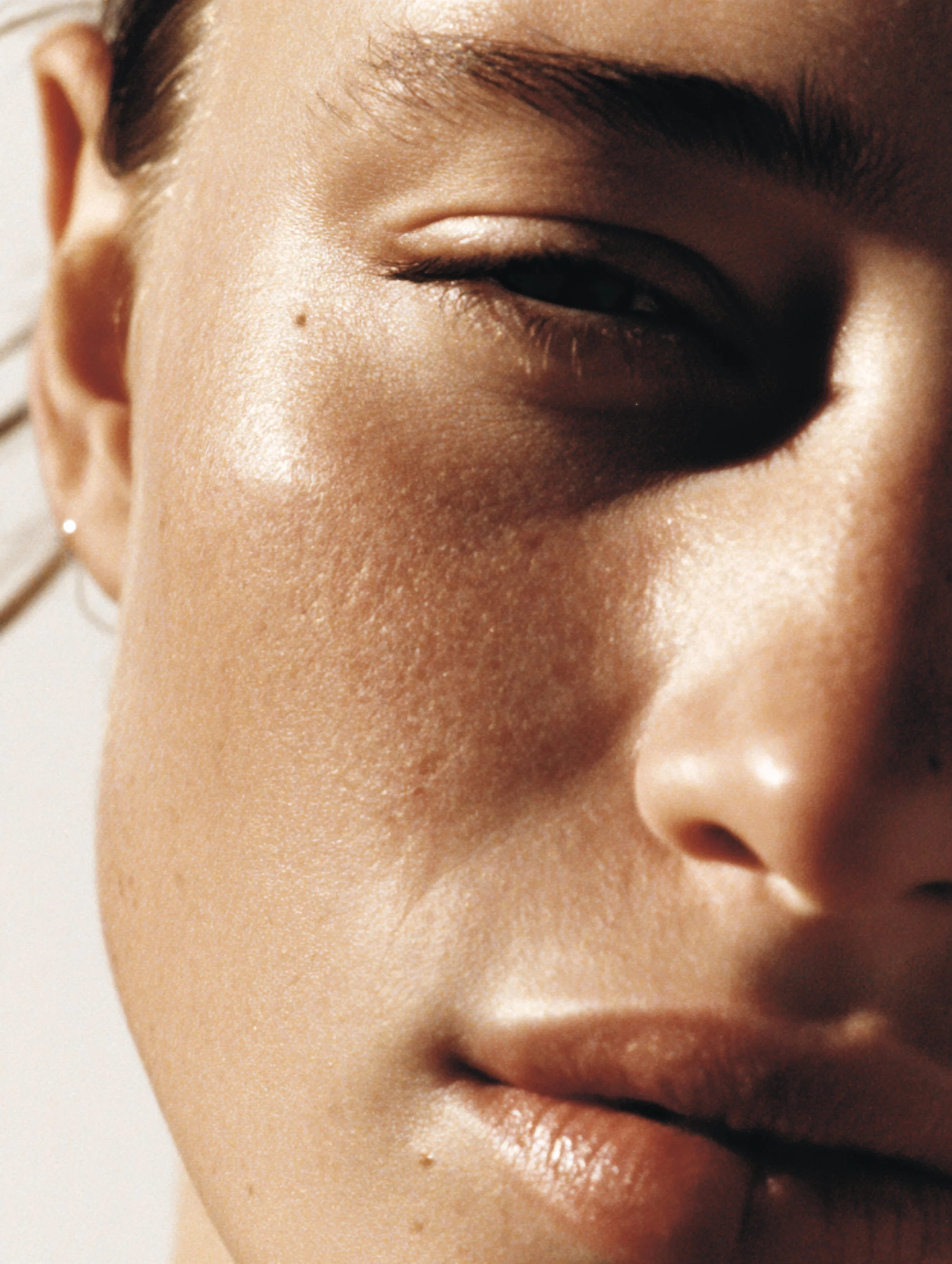Close-up of a person's face focusing on the eye, cheek, and lips, with shiny skin and minimal makeup.