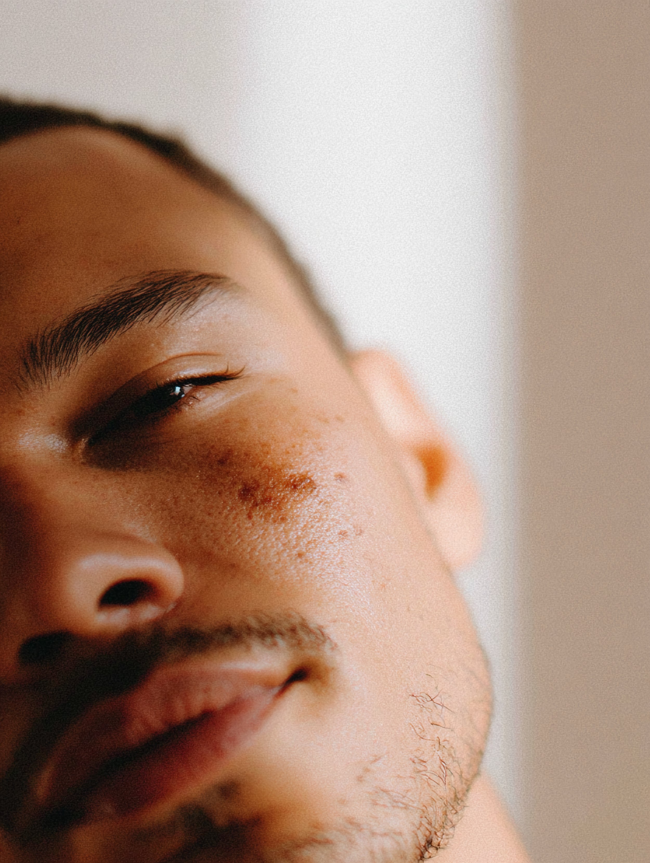 Close-up of a young man's face with partially closed eyes, showing facial hair and skin texture.