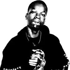 Portrait of a man with a serious expression, wearing a dark hoodie and necklace, with short hair and facial hair.