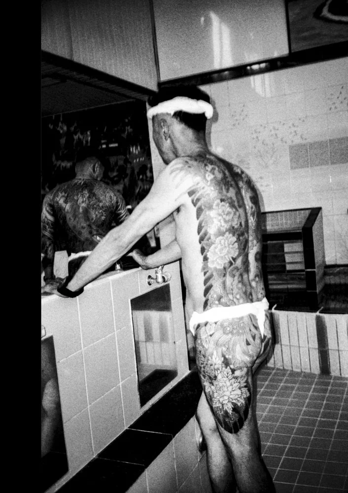 Black and white portrait of a standing and heavily tattooed Yakuza member from the back.