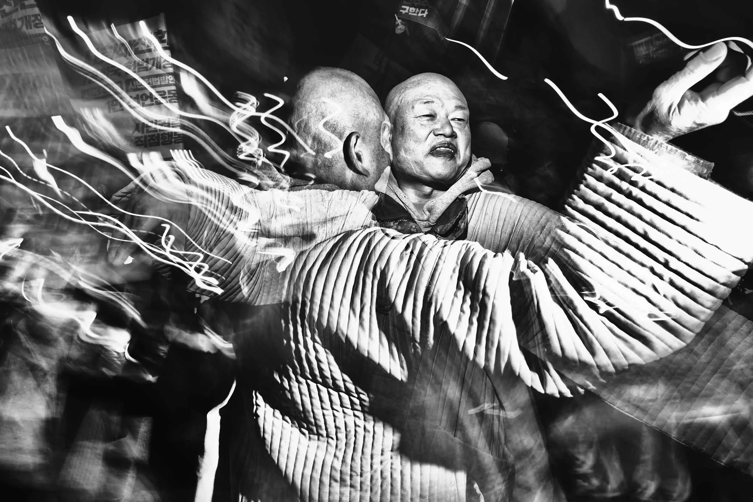 A Buddhist dances to pungmul protest music in the night air on a street adjacent to Gwanghwamun Gate during an anti-Yoon march in Seoul.