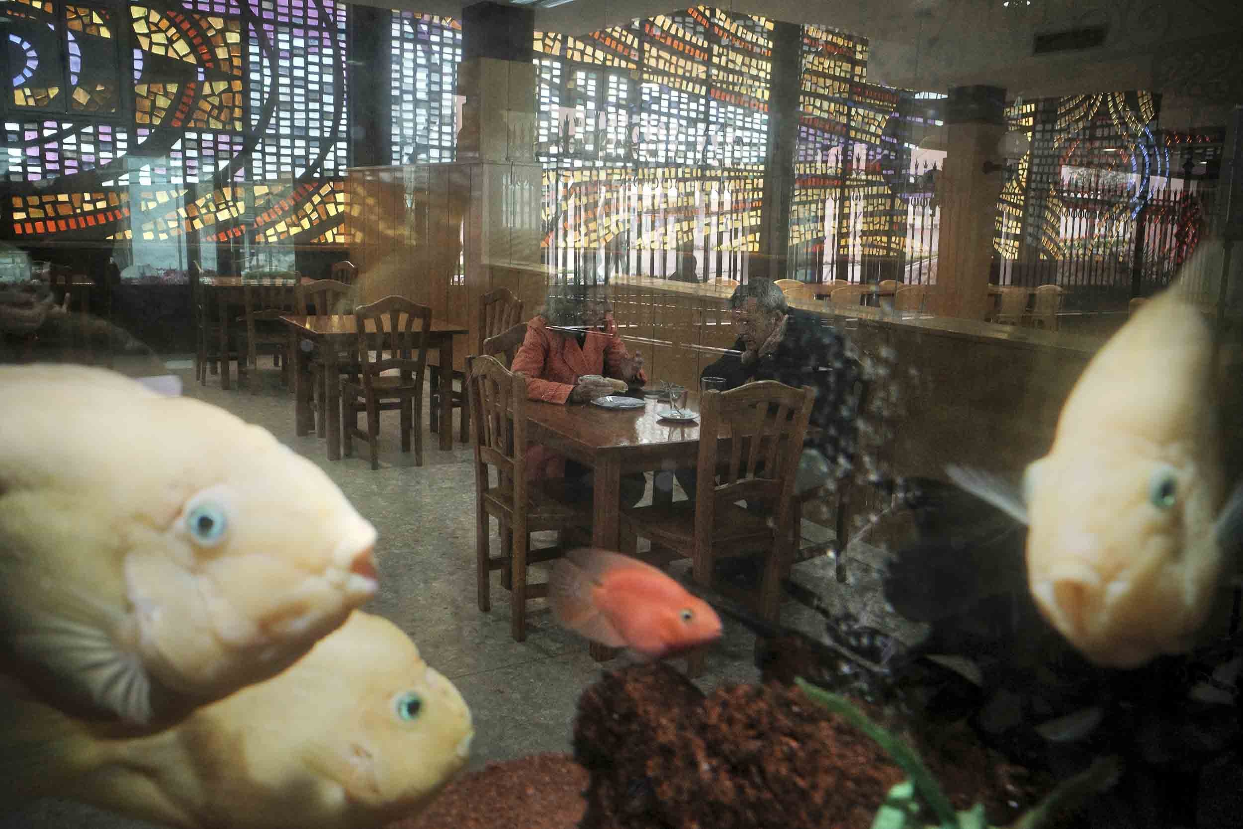 A couple seated at a restaurant table shot through a fish bowl and fish there in the foreground.