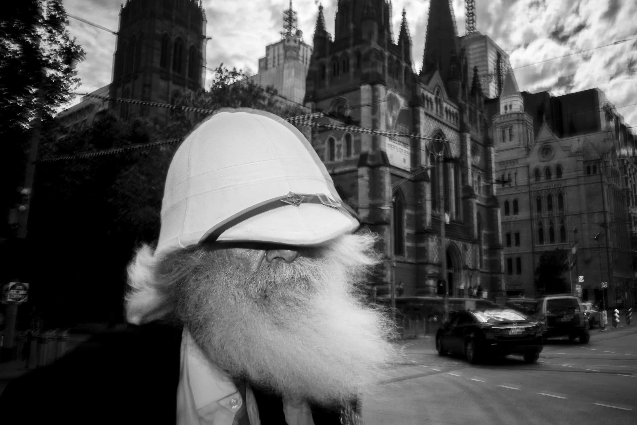 Black and white photograph of a gentleman in a weird hat walking past the camera.