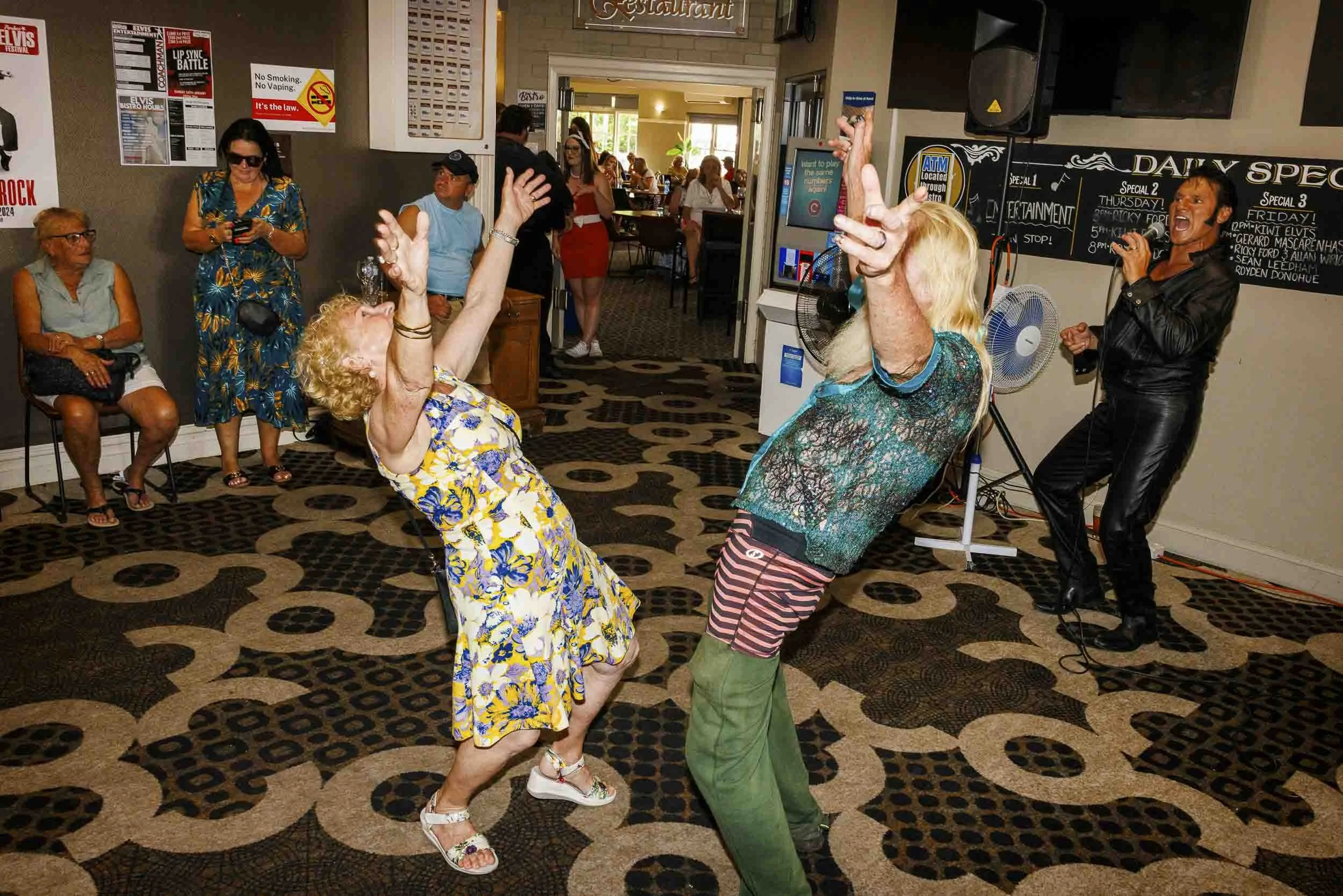 An elderly man and lady throwing their hands in the air and dancing as Elvis impersonator Ricky Graceland serenades them at the Parkes Elvis Festival.